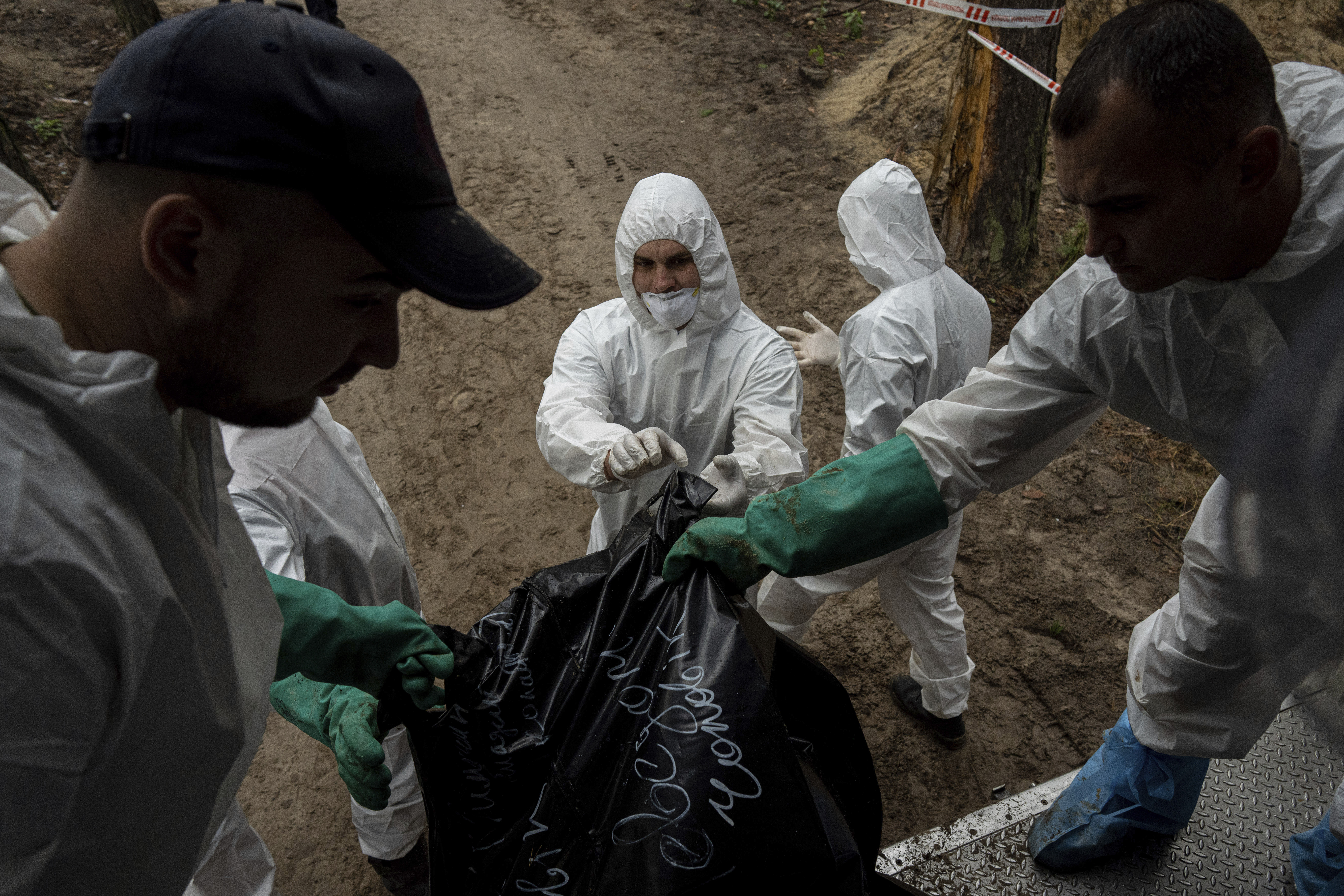 Emergency workers load a body into a refrigerator truck in a cemetery after exhumation in the recently retaken area of Izium, Ukraine, Friday, Sept. 23, 2022. (AP Photo/Evgeniy Maloletka)