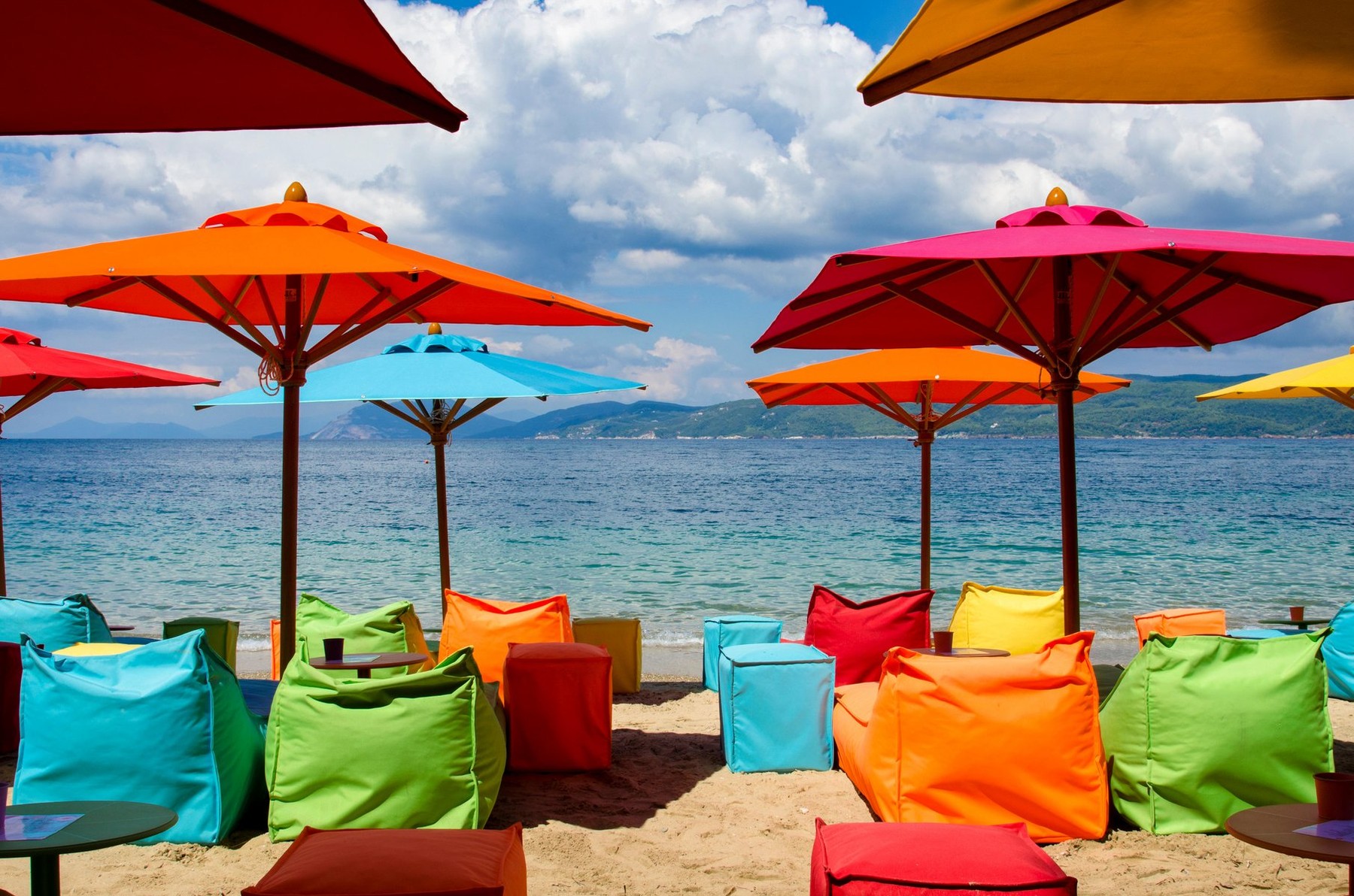 Modern beach equipped with umbrellas, and multicolored inflatable deckchairs for trendy tourists, Skiathos Greece, at the bottom the sea and a cloudy