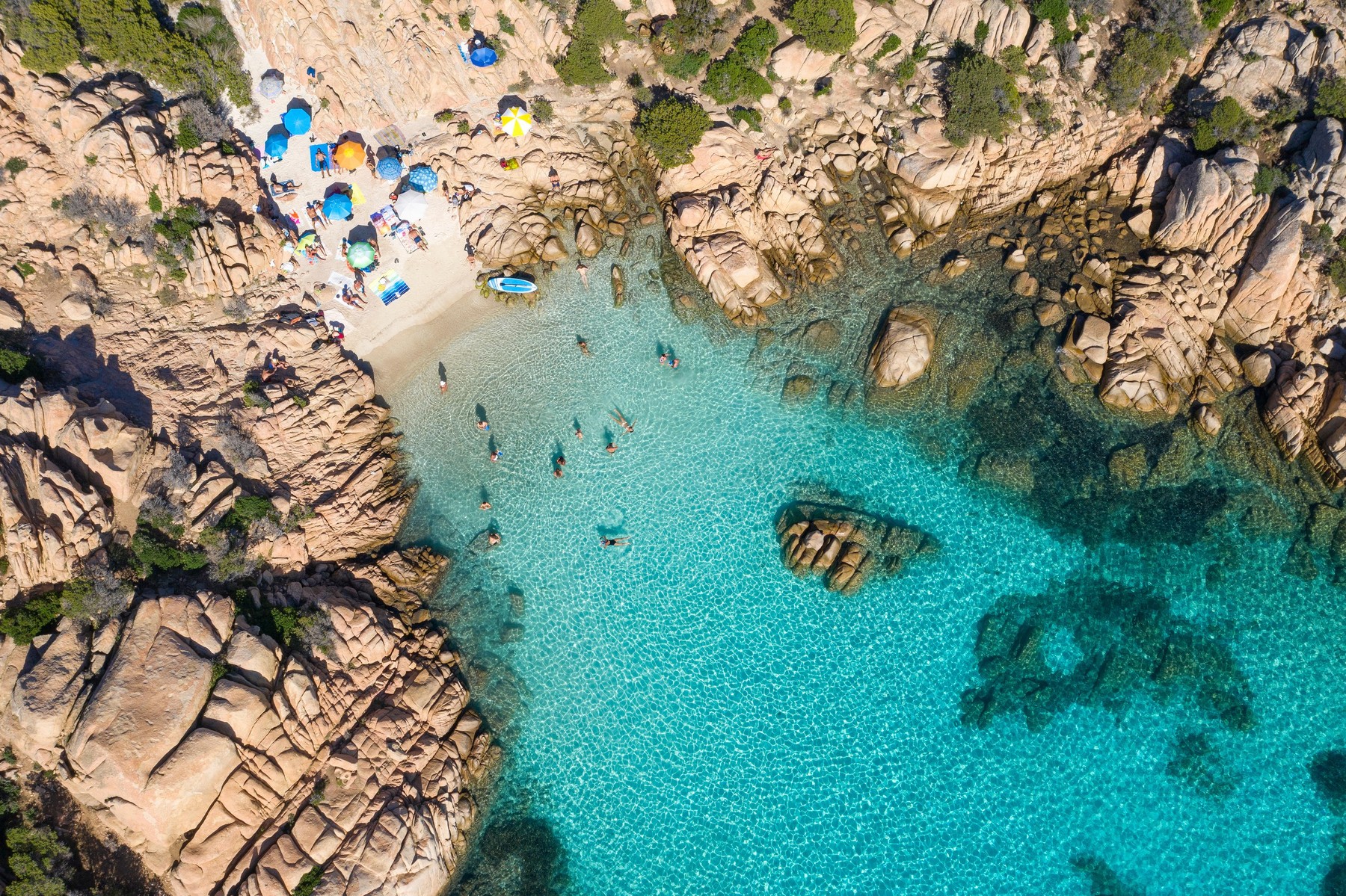 View from above, stunning aerial view of a small beach with beach umbrellas and people swimming in a turquoise clear water, Cala Coticcio, (Tahiti)