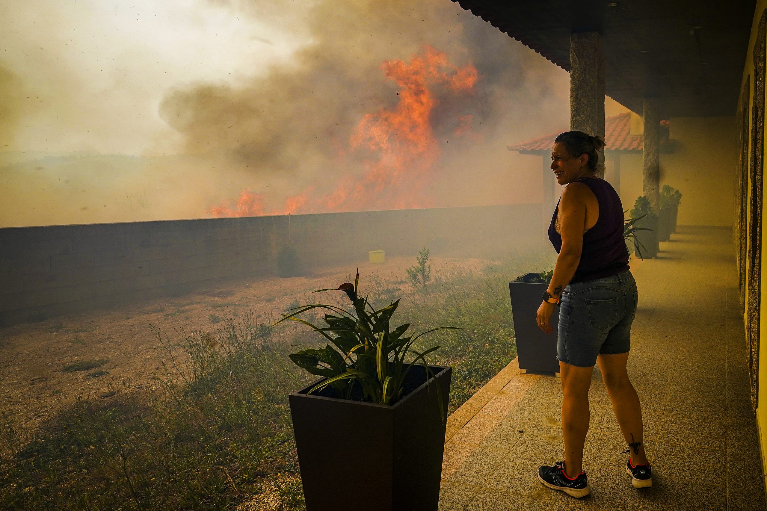 epa10072750 A local woman looks at the flames burning trees surrounding her house in Ancede village during a wildfire in the municipality of Baiao, North of Portugal, 15 July 2022.  EPA-EFE/HUGO DELGADO