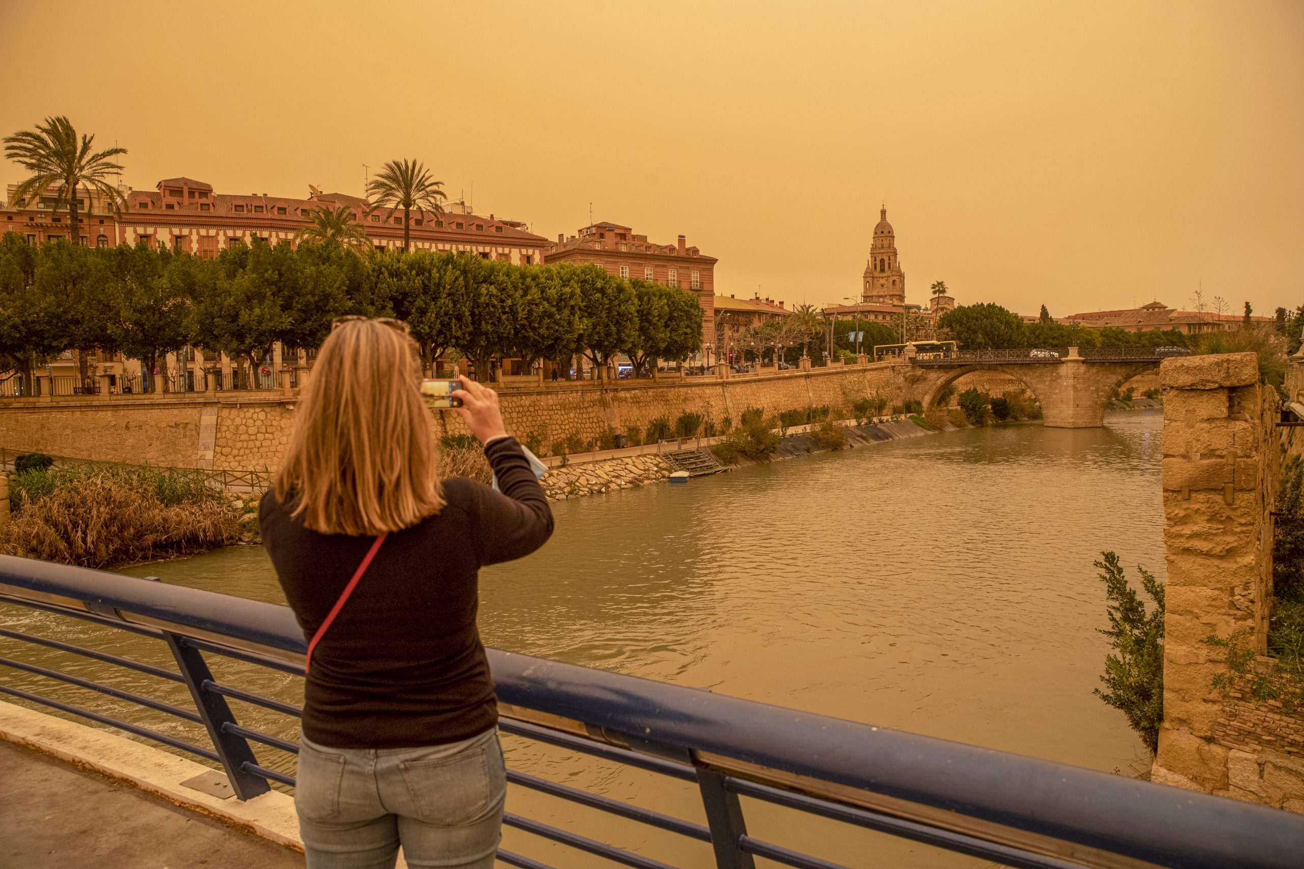 epa09824770 A woman takes a photo with her mobile of the downtow of Murcia orange-blanketed with heavy dust, in Spain, 14 March 2022. Spanish State weather agency AEMET forecasts cloudy sky with no rain in the region.  EPA-EFE/Marcial Guillen