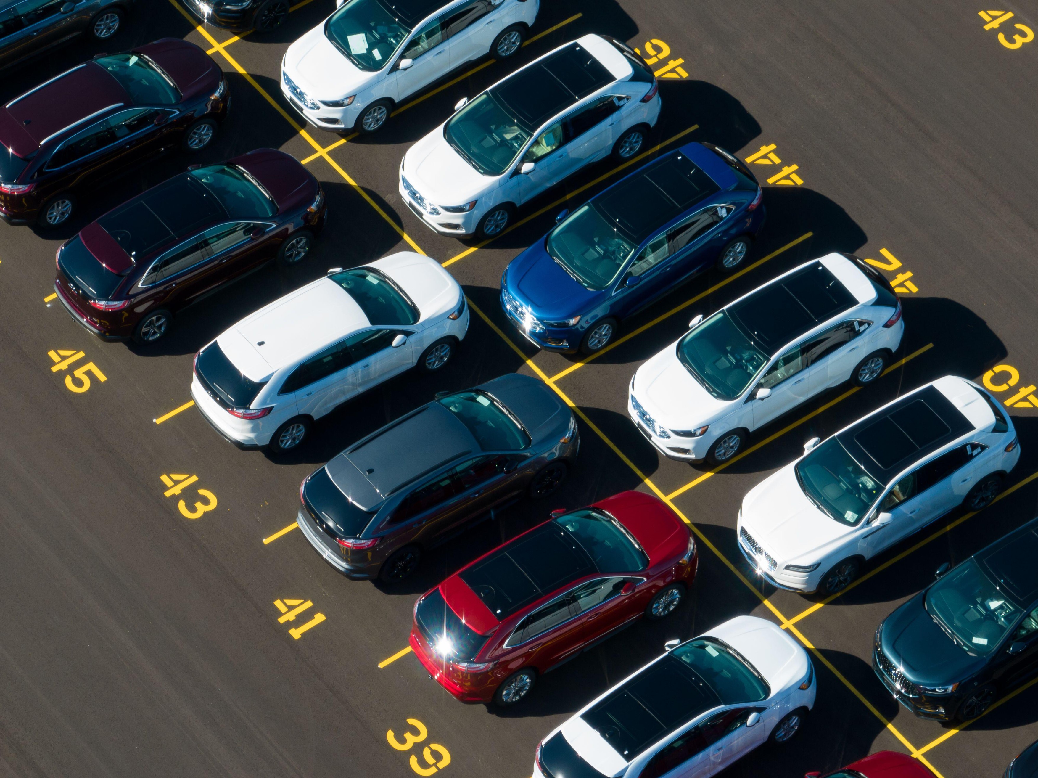 An aerial view above a parking lot at a Ford Motor Company plant. Rows of newly manufactured Ford Edge SUVs are seen on a sunny day.
