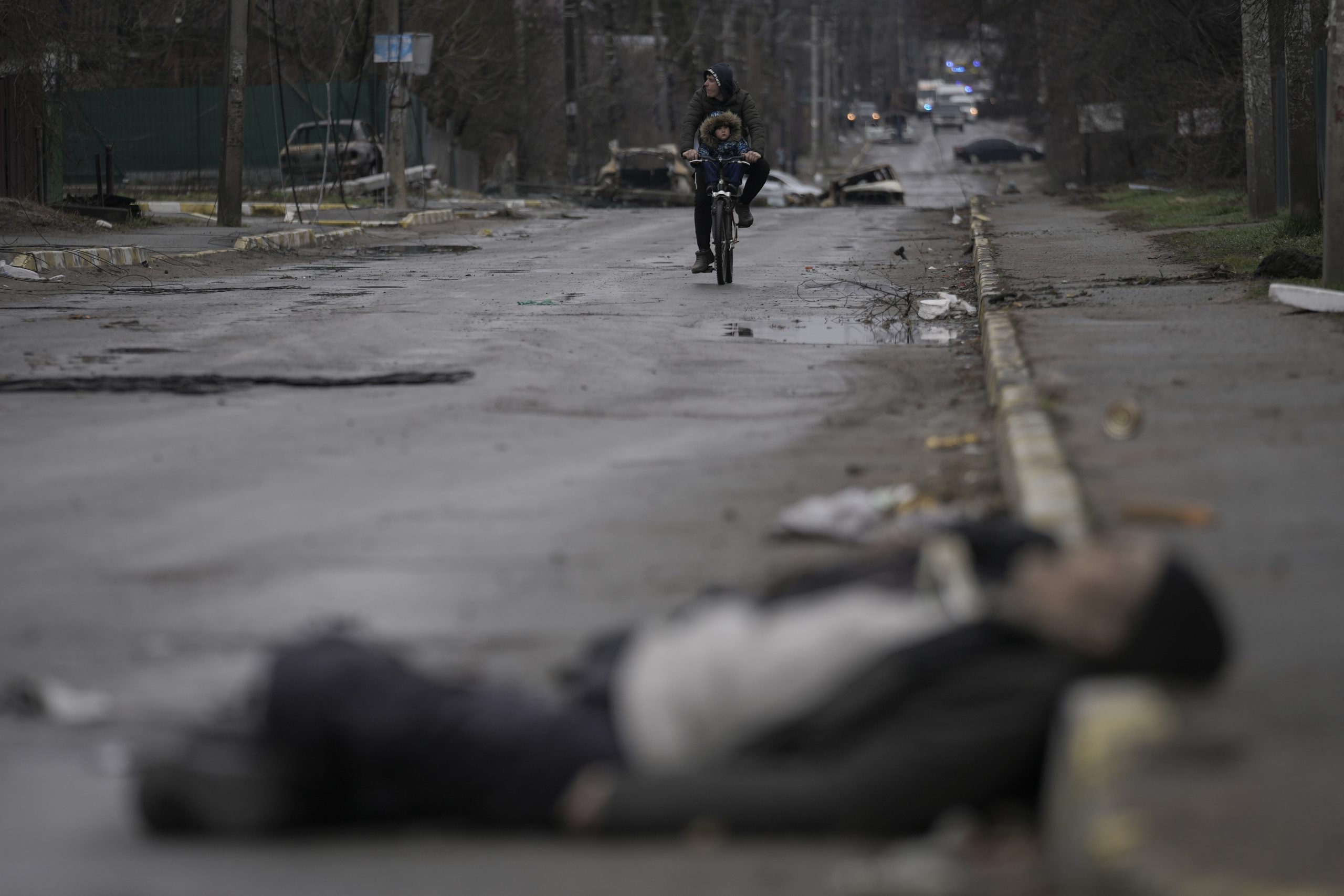 A man and child on a bicycle come across the body of a civilian lying on a street in the formerly Russian-occupied Kyiv suburb of Bucha, Ukraine, Saturday, April 2, 2022. (AP Photo/Vadim Ghirda)