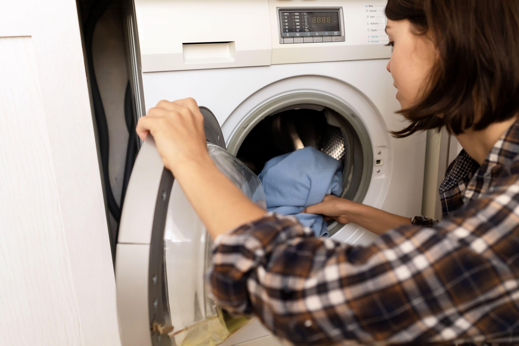 Woman puts bright clothes into a washing machine.