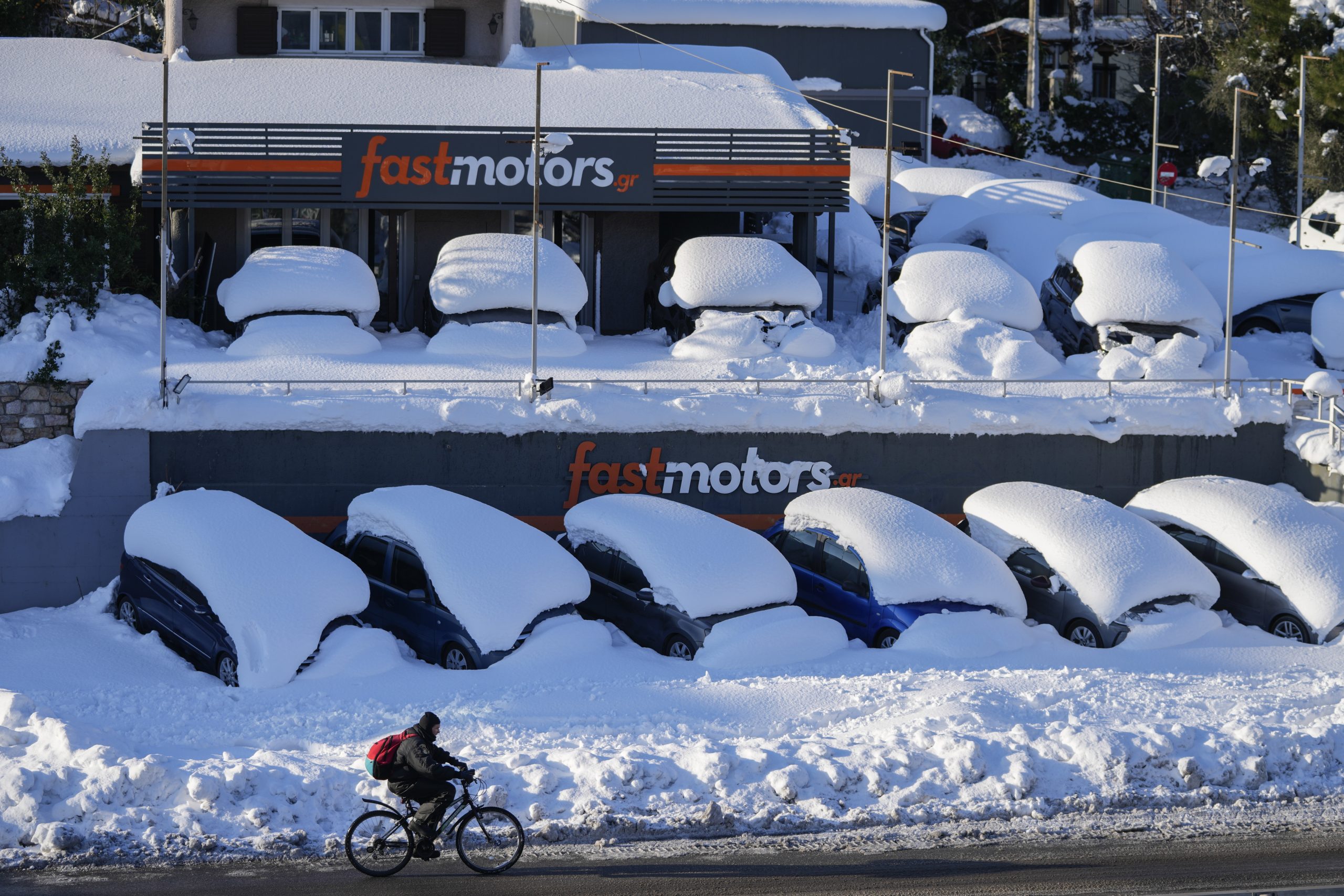 A cyclist passes in front of cars covered with snow in northern Athens following Tuesday's heavy snowfall, on Wednesday, Jan. 26, 2022. (AP Photo/Thanassis Stavrakis)