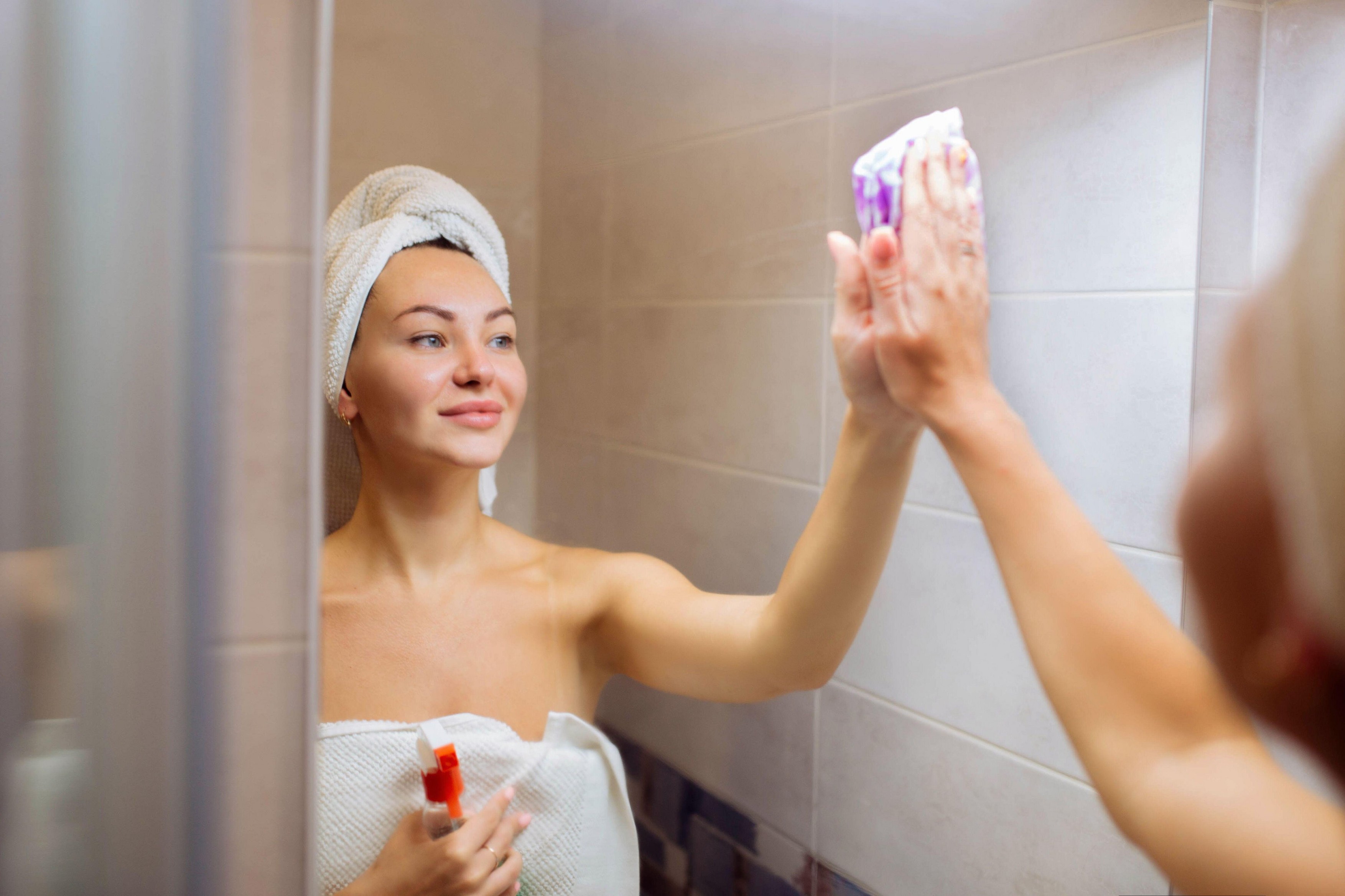 Cleaning in the shower room. A beautiful girl washes the mirror with a rag