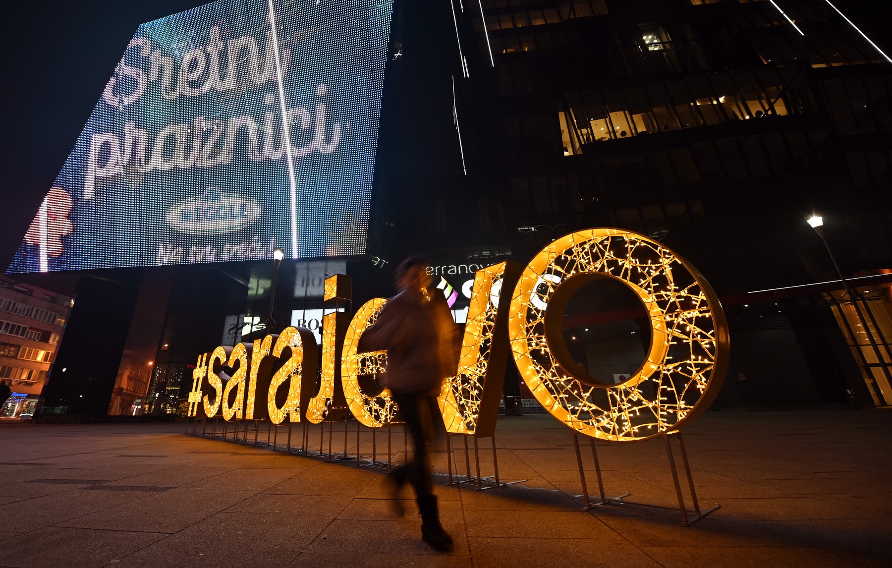 People walk past a lit-up sign reading "#Sarajevo", outside a shopping center, late on December 31, 2021.,Image: 650053258, License: Rights-managed, Restrictions: , Model Release: no, Credit line: ELVIS BARUKCIC / AFP / Profimedia