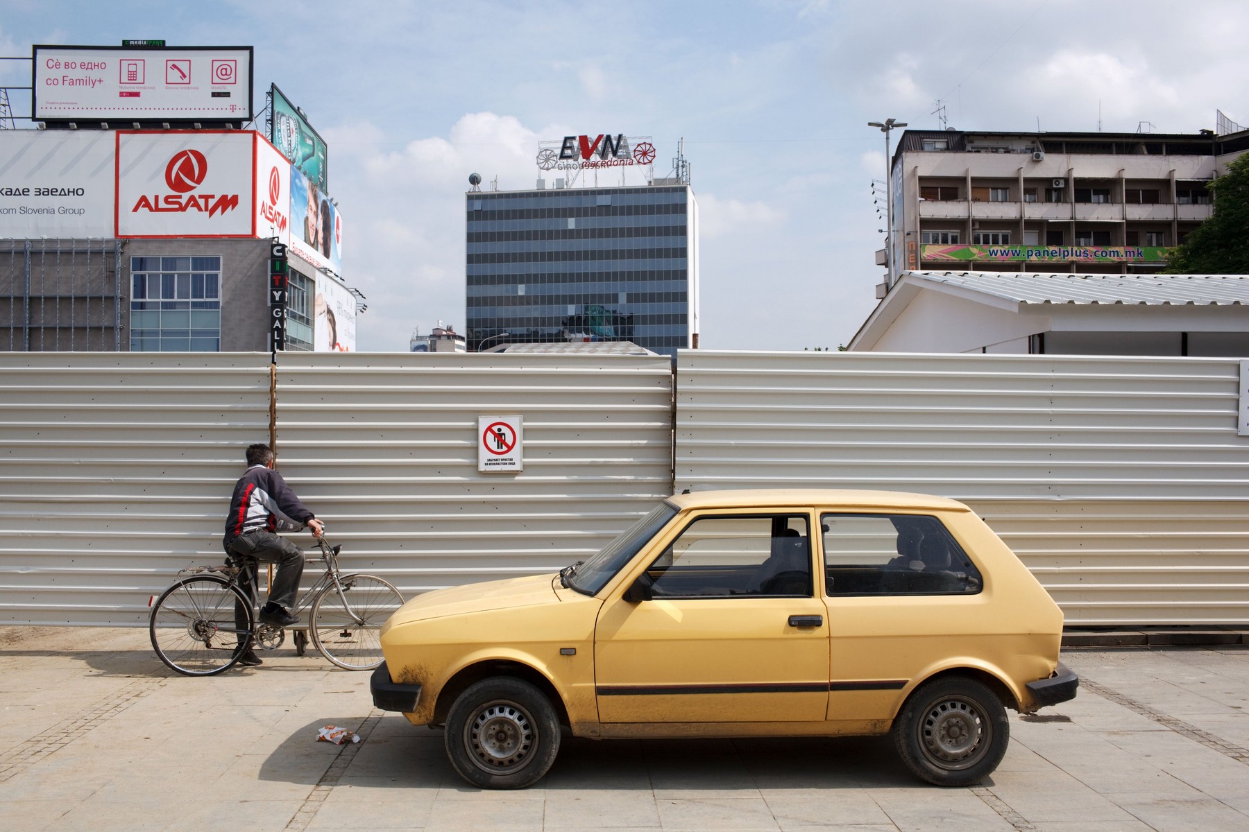 A man on a bicycle and yellow Yugo car parked in central Skopje, Macedonia.