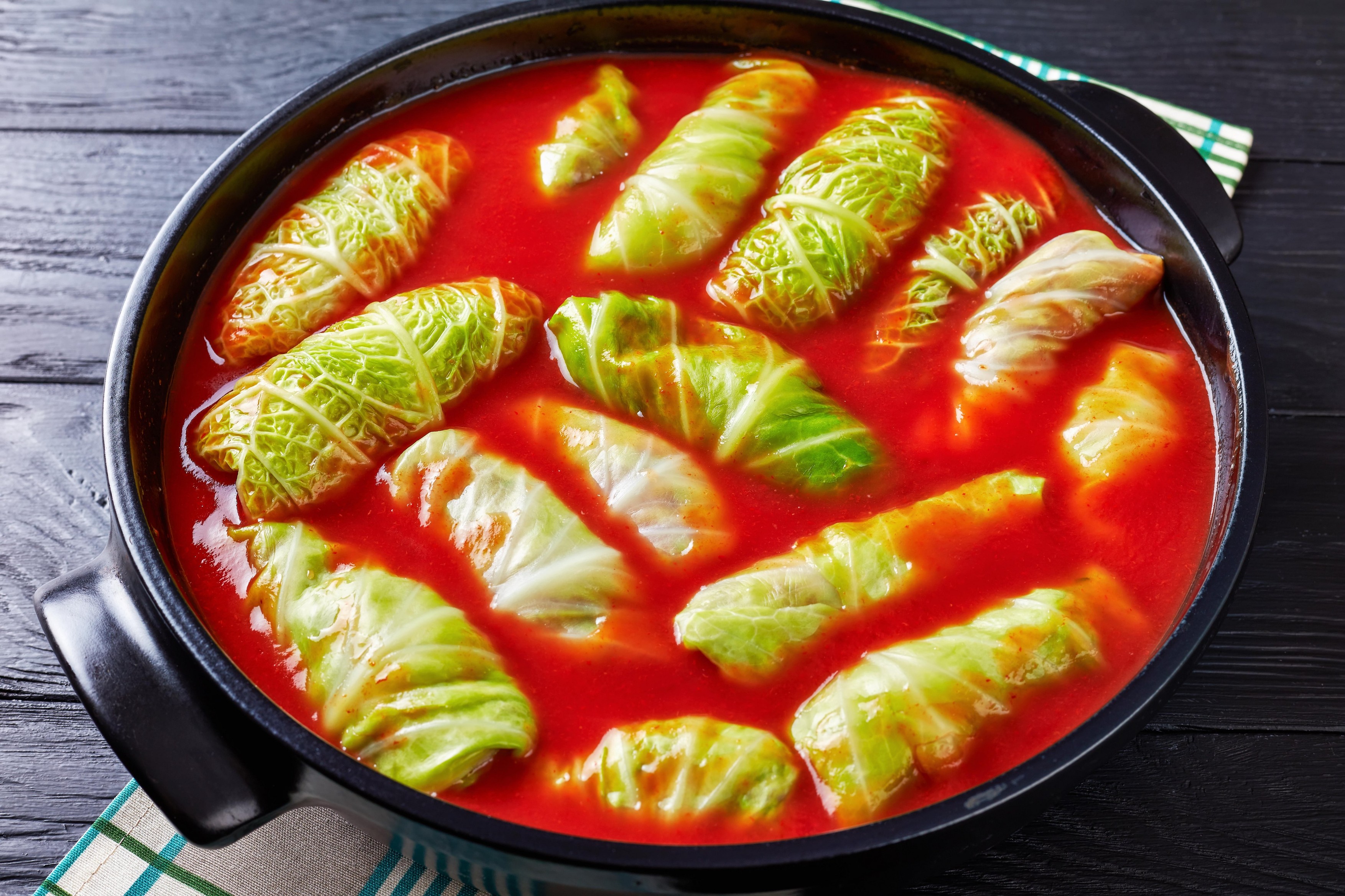 overhead view of raw cabbage leaves rolls stuffed with minced beef, boiled rice prepared to cook with tomato sauce in dutch oven, view from above, clo