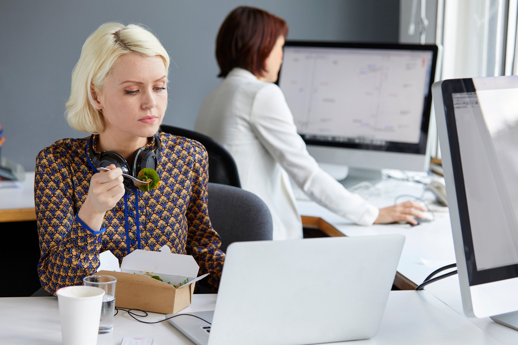 Female designer looking at laptop during working lunch at office desk