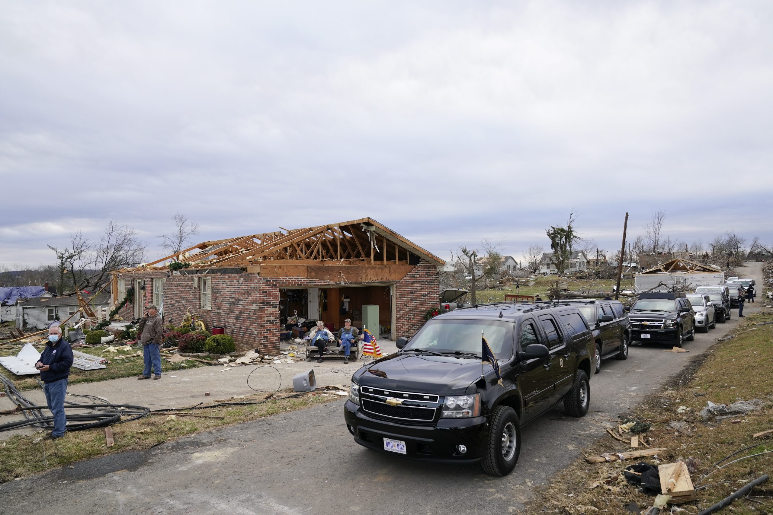 People sit near President Joe Biden's motorcade as Biden surveys storm damage from tornadoes and extreme weather in Dawson Springs, Ky., Wednesday, Dec. 15, 2021. (AP Photo/Andrew Harnik)
