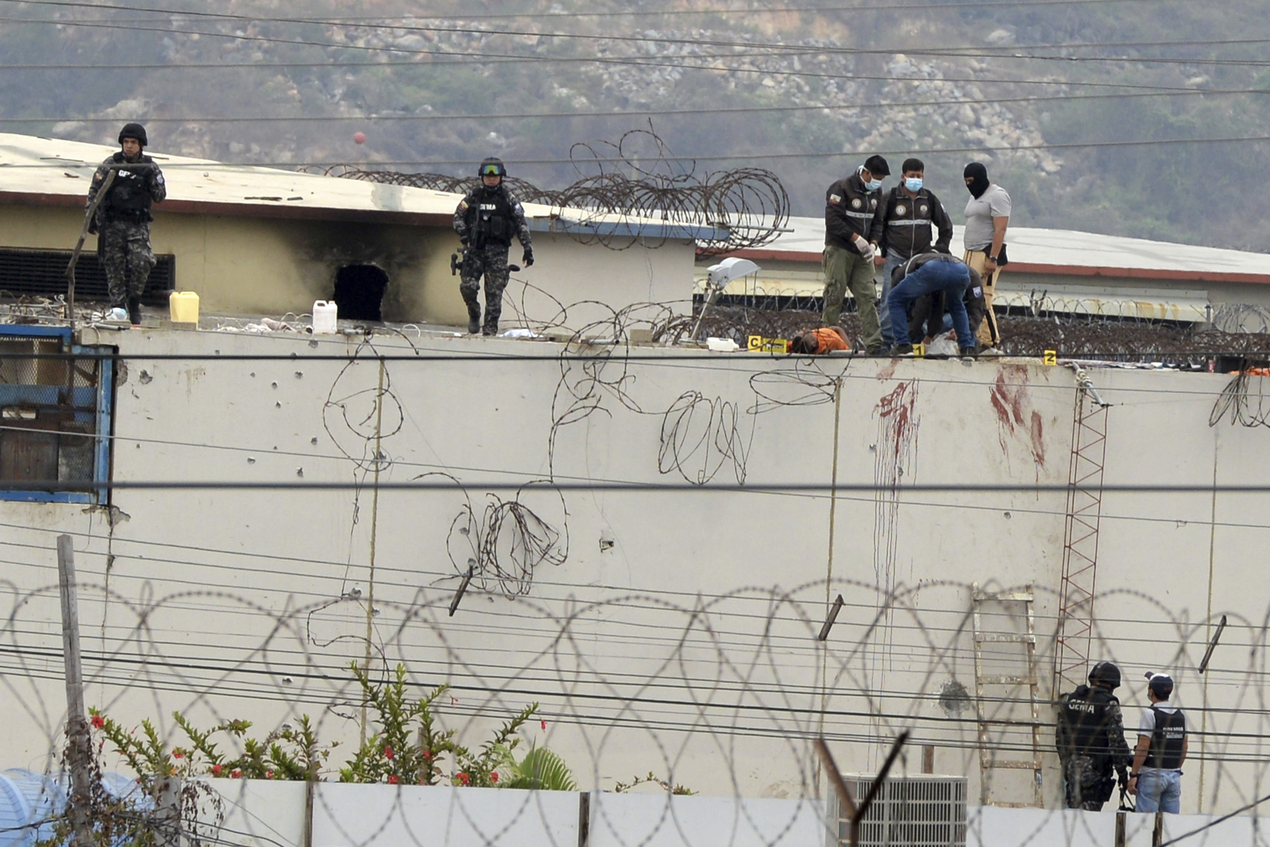 The body of a prisoner appears surrounded by police on the roof of the Litoral penitentiary the morning after riots broke out inside the jail in Guayaquil, Ecuador, Saturday, Nov. 13, 2021. (AP Photo/Jose Sanchez)