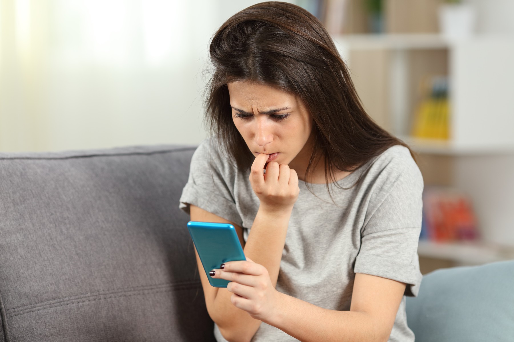 Nervous girl biting nails reading phone content sitting on a couch in the living room at home,Image: 528541890, License: Royalty-free, Restrictions: , Model Release: yes, Credit line: Antonio Guillen Fernández / Panthermedia / Profimedia