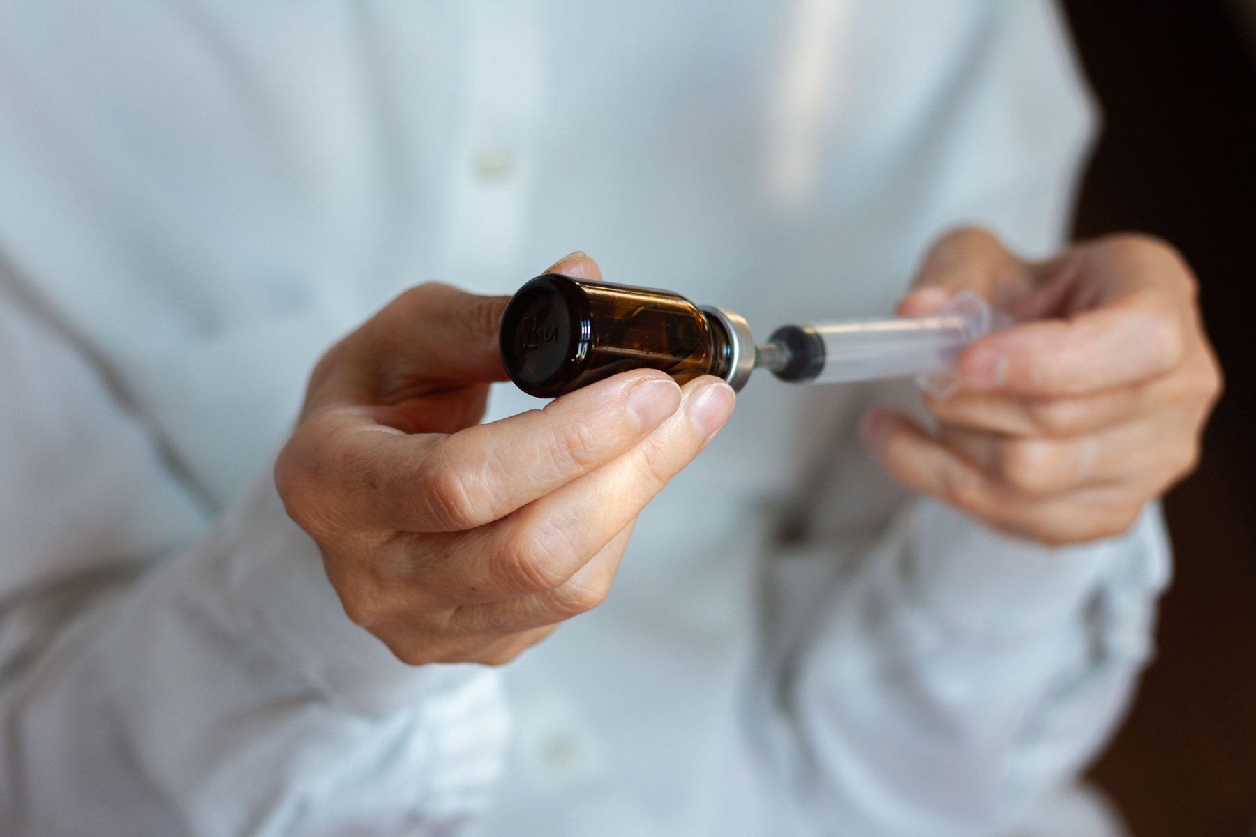 doctor in a white surgical gown and blue mask holds in hands a medical syringe and bottle with medicine for injection. Insulin resistance, diabetes pr
