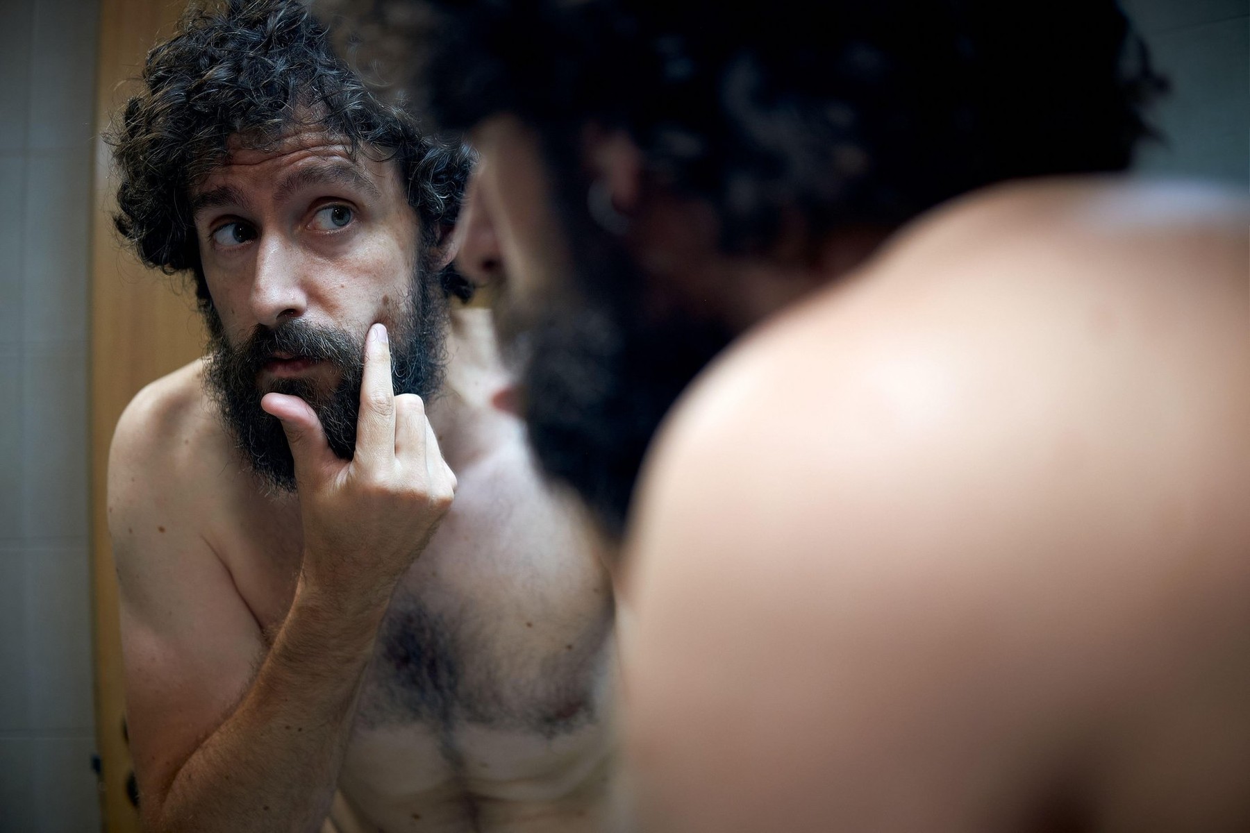 Middle-aged hispanic man examines a mole he has in his cheek.