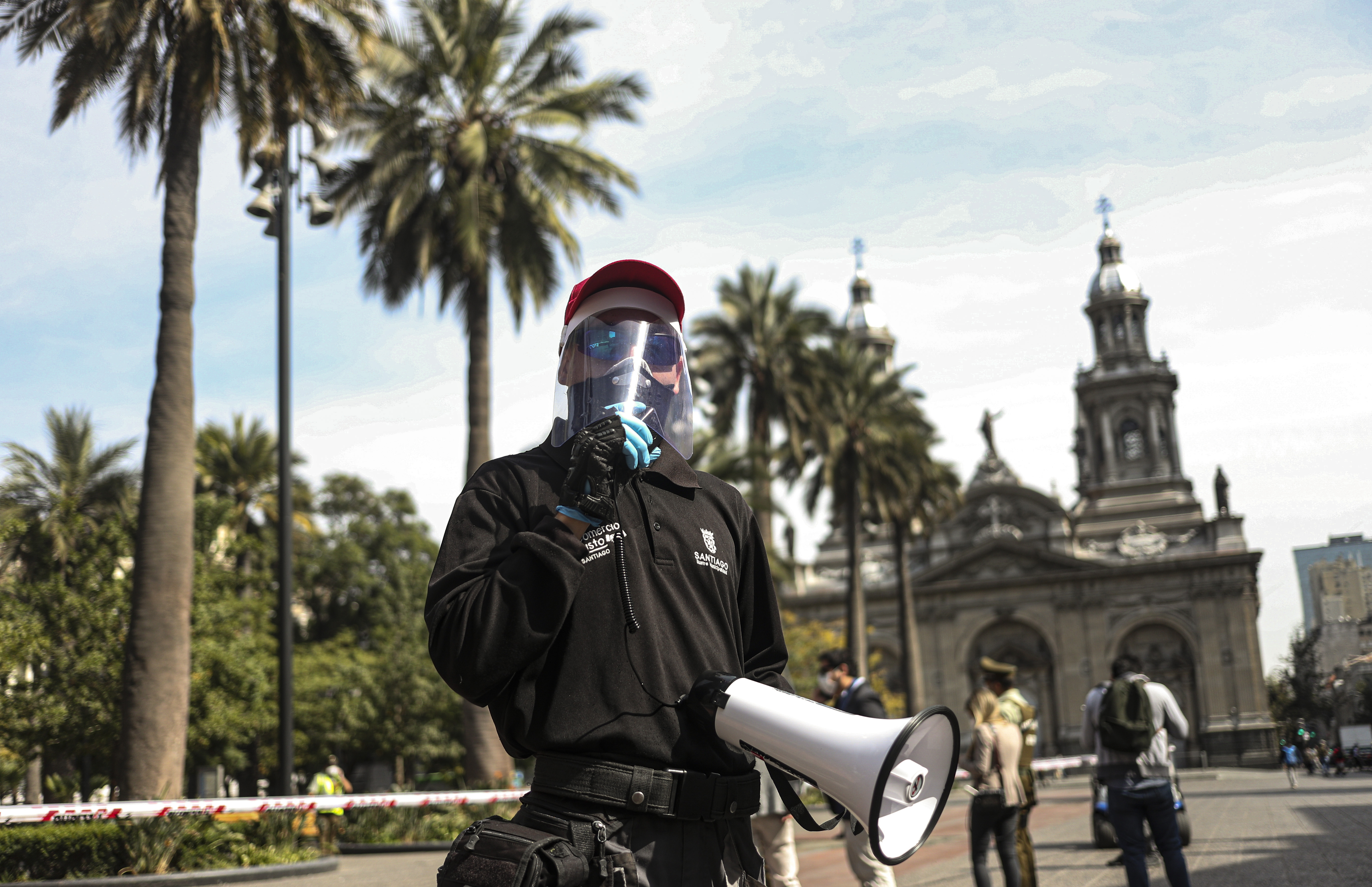 A city worker wearing protective gear as a precaution against the new coronavirus, uses a megaphone to announce to pedestrians in the Plaza de Armas that the city is under quarantine, in Santiago, Chile, Wednesday, April 15, 2020. (AP Photo/Esteban Felix)
