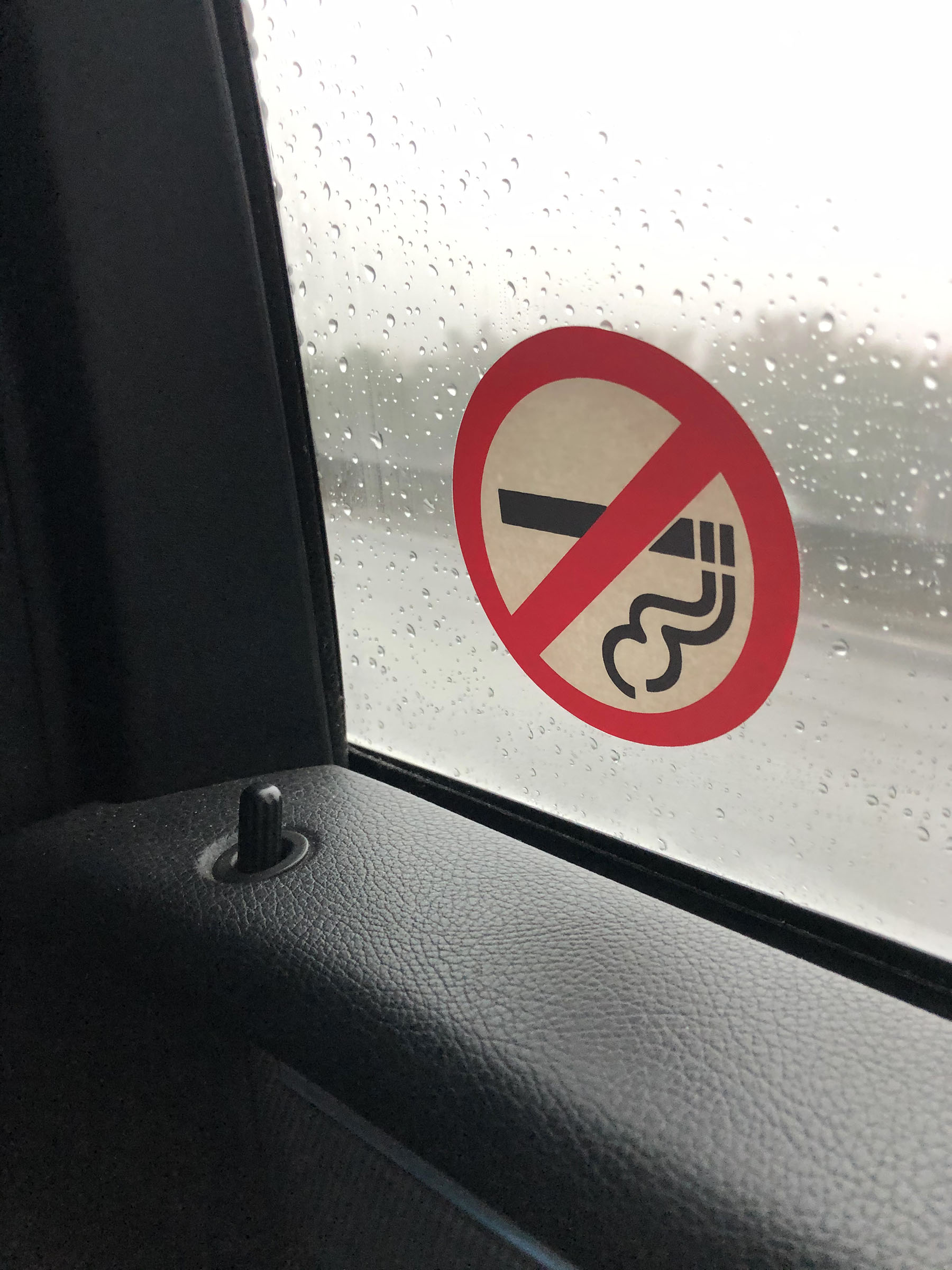 Stock photo showing the view from the interior of a taxicab driving through rain, No smoking symbol sign on passenger window