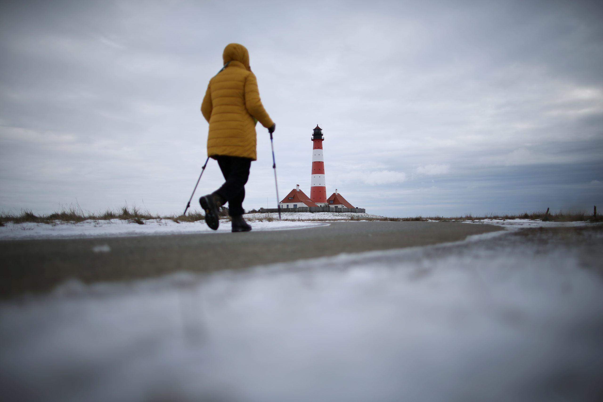 06022021 A walker with sticks walks towards a lighthouse in Westerhever, Germany, February 6, 2021.     REUTERS/Cathrin Mueller