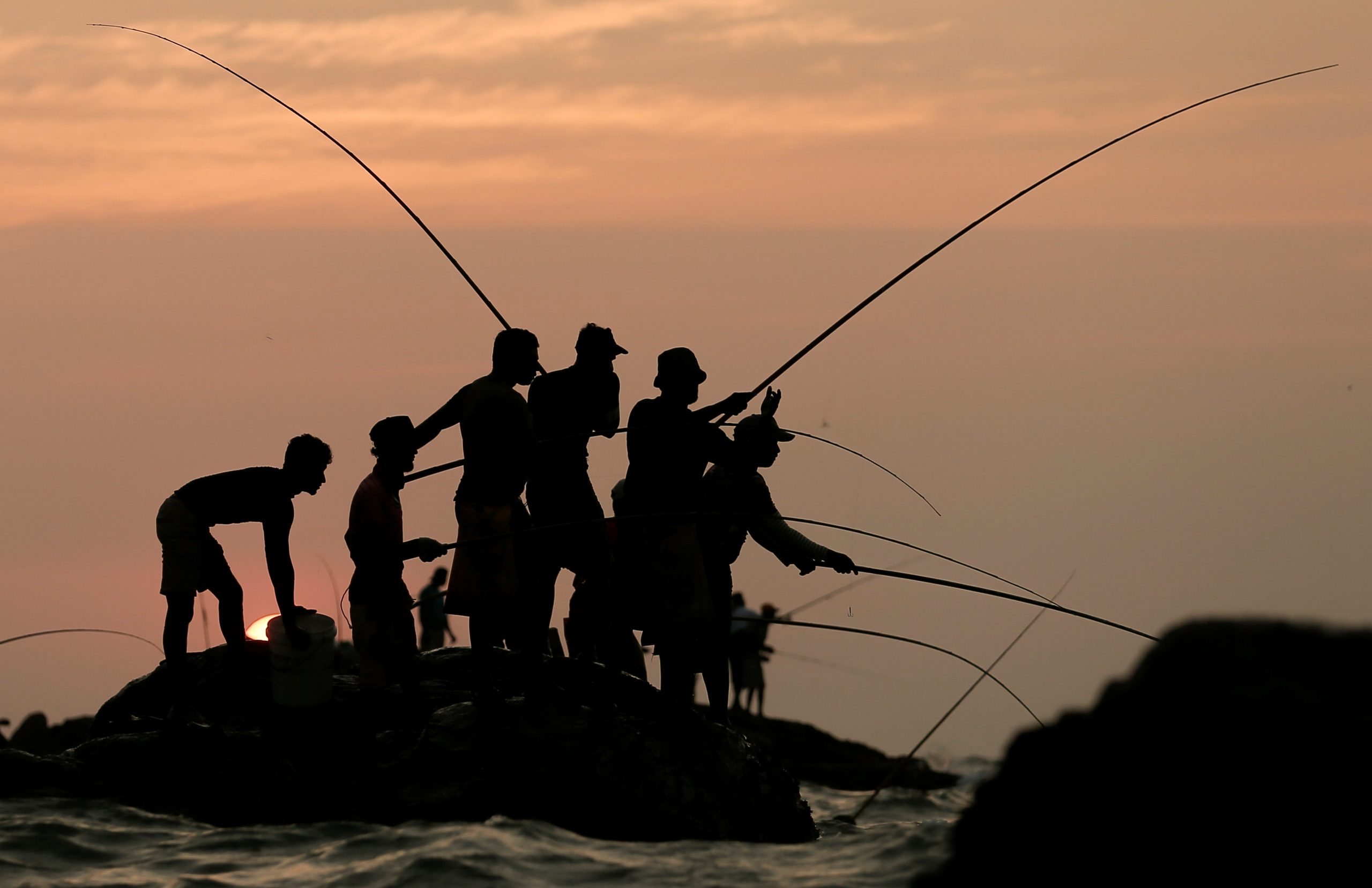 10022021 Men hold fishing rods wait for their catch on top of a rock in the sea in Colombo, Sri Lanka February 10, 2021. REUTERS/Dinuka Liyanawatte