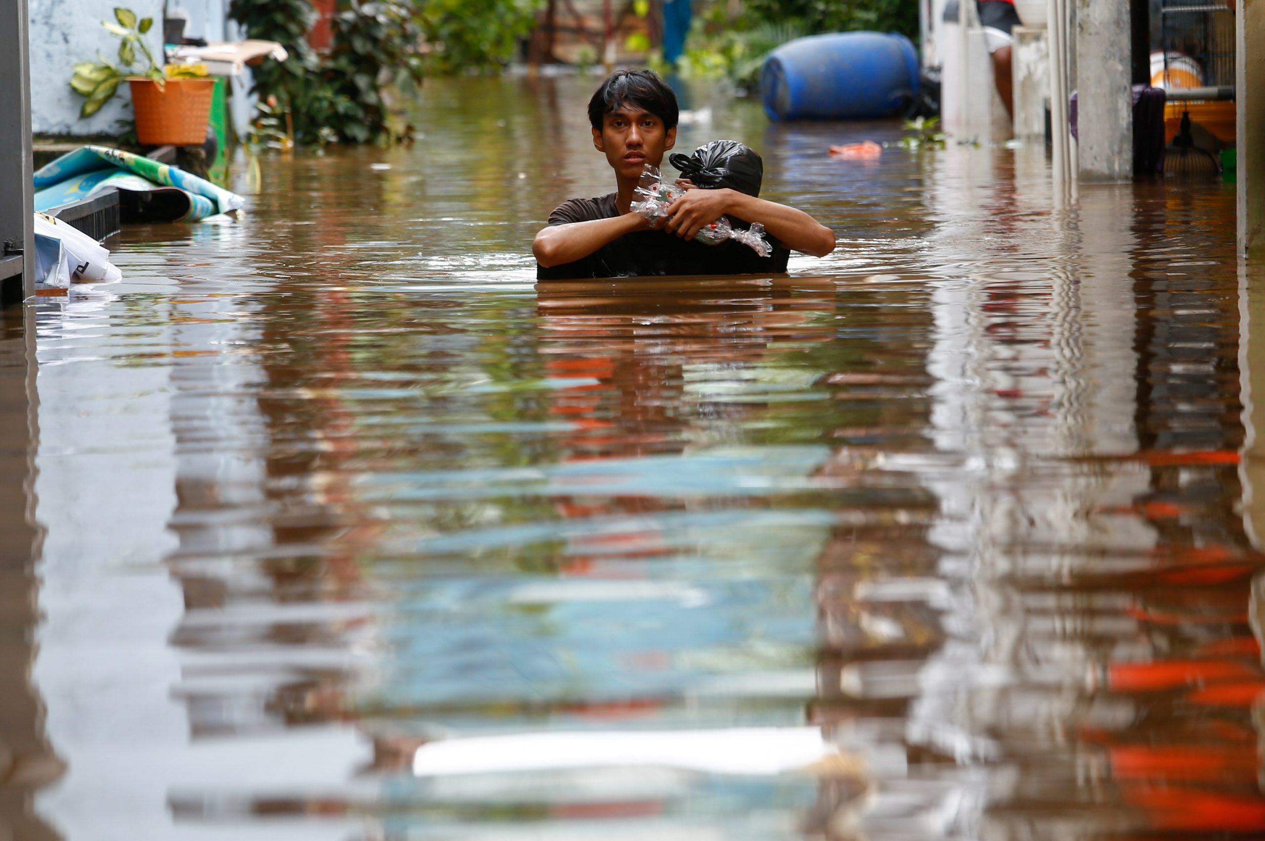 20022021 A man carrying his goods walks through the water in an area affected by floods, following heavy rains in Jakarta, Indonesia, February 20, 2021. REUTERS/Ajeng Dinar Ulfiana