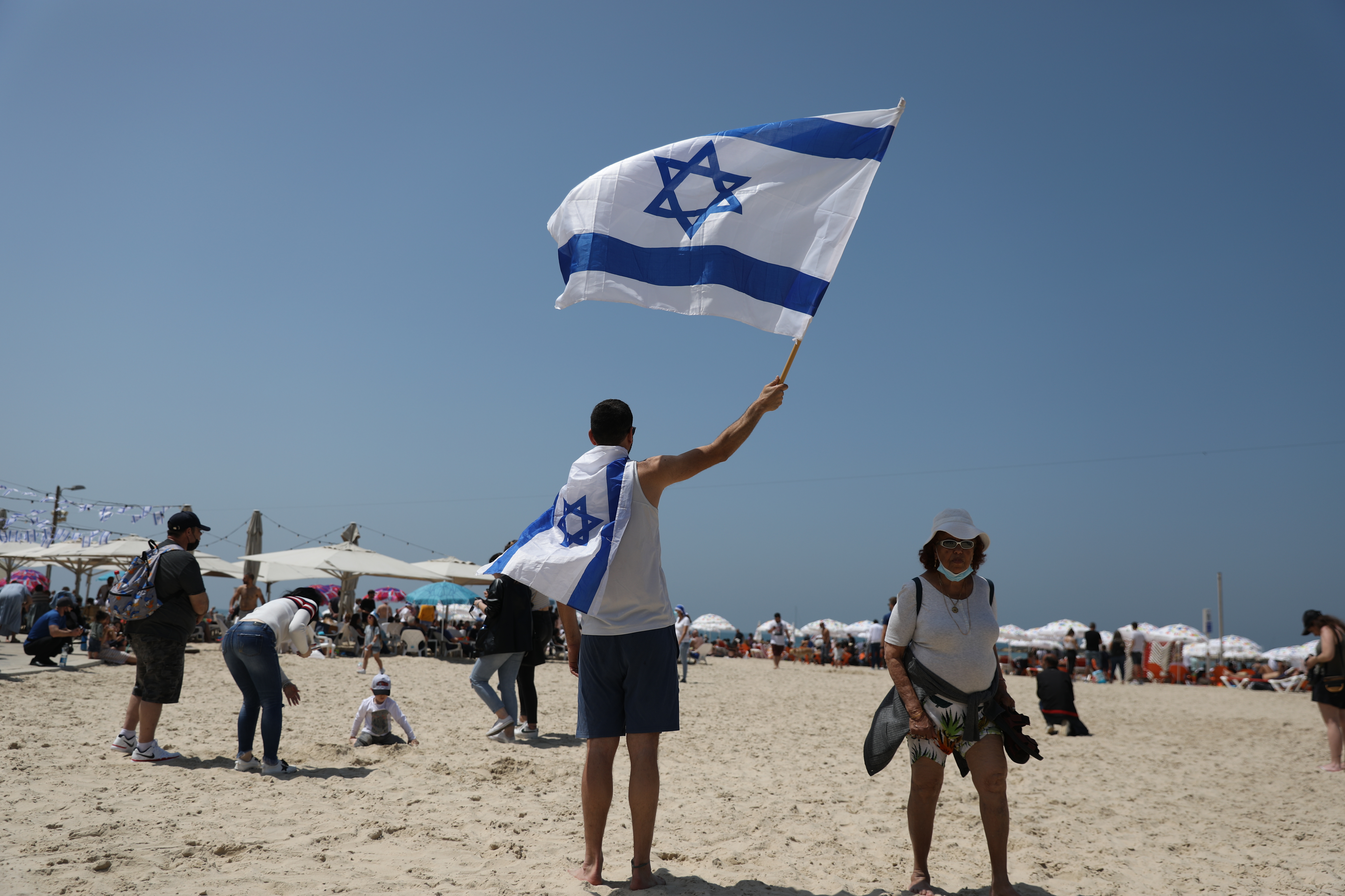 epa09136489 A man waves the flag if Israel during the Independence Day celebrations at a beach of Tel Aviv, Israel, 15 April 2021. Israeli Independence Day marks the 73th anniversary of the creation of the Jewish state in 1948.  EPA-EFE/ABIR SULTAN
