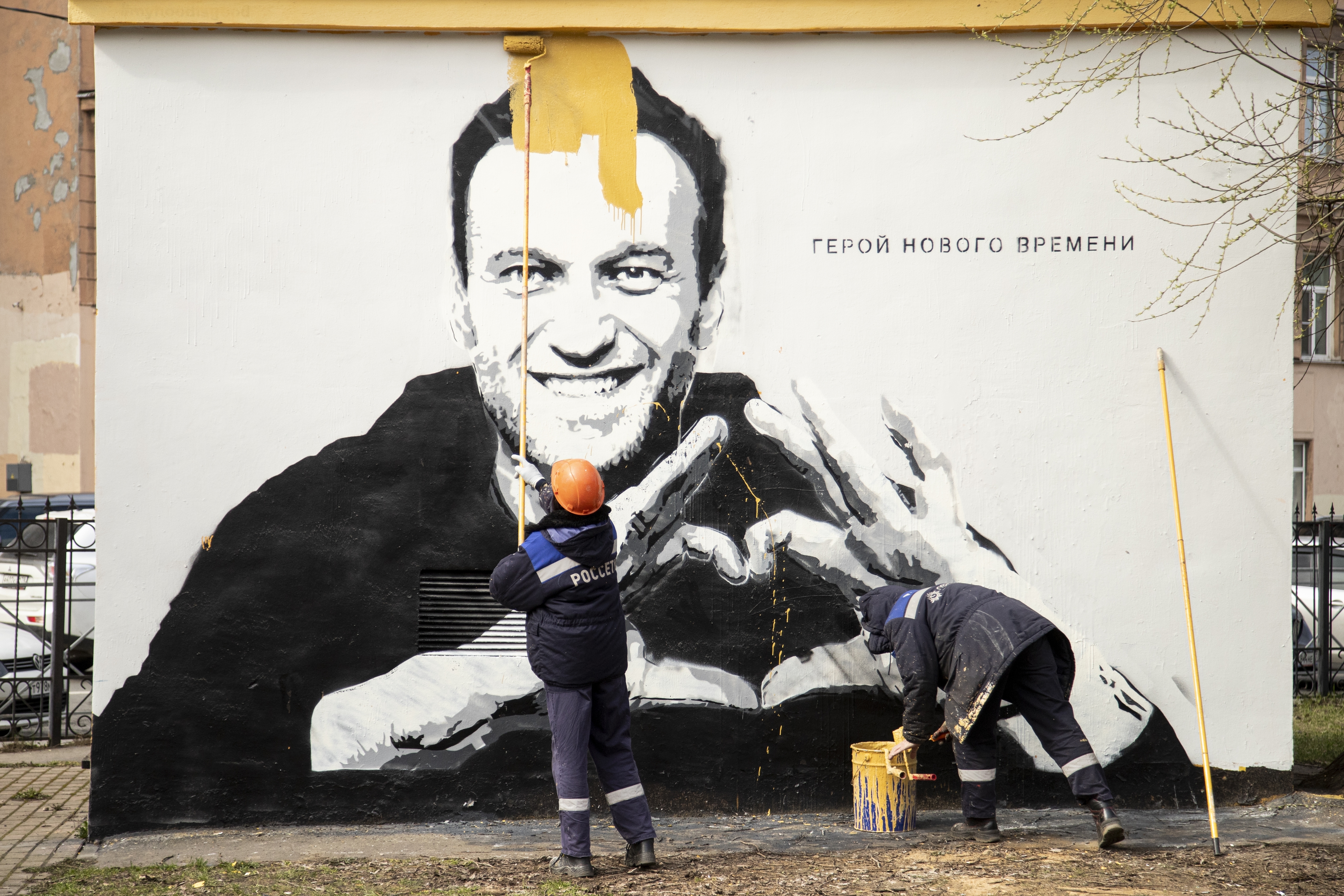 Municipal workers paint over graffiti of Russia's imprisoned opposition leader Alexei Navalny in St. Petersburg, Russia, Wednesday, April 28, 2021. The worlds on the wall reading "Hero of our time". (AP Photo/Ivan Petrov)