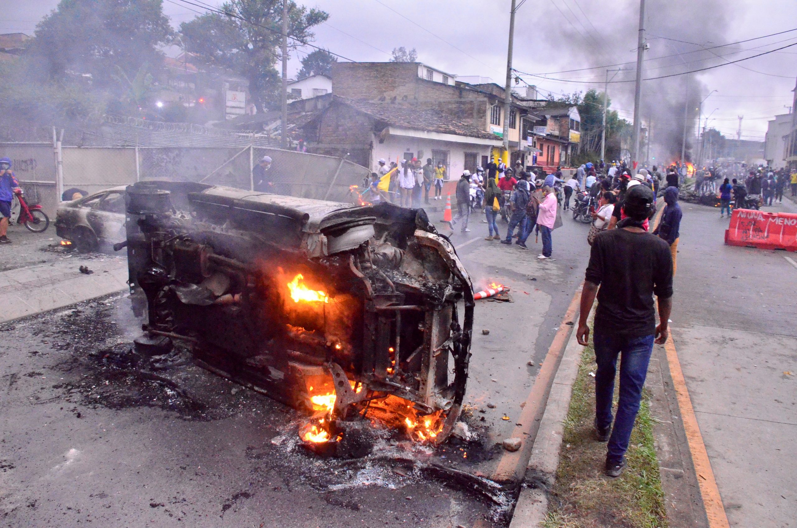 epa09234468 People walk past a burning car at a parking lot in Popayan Colombia, 28 May 2021. Colombia marks one month of continuous protests against the government and police brutality.  EPA-EFE/Mario Parra