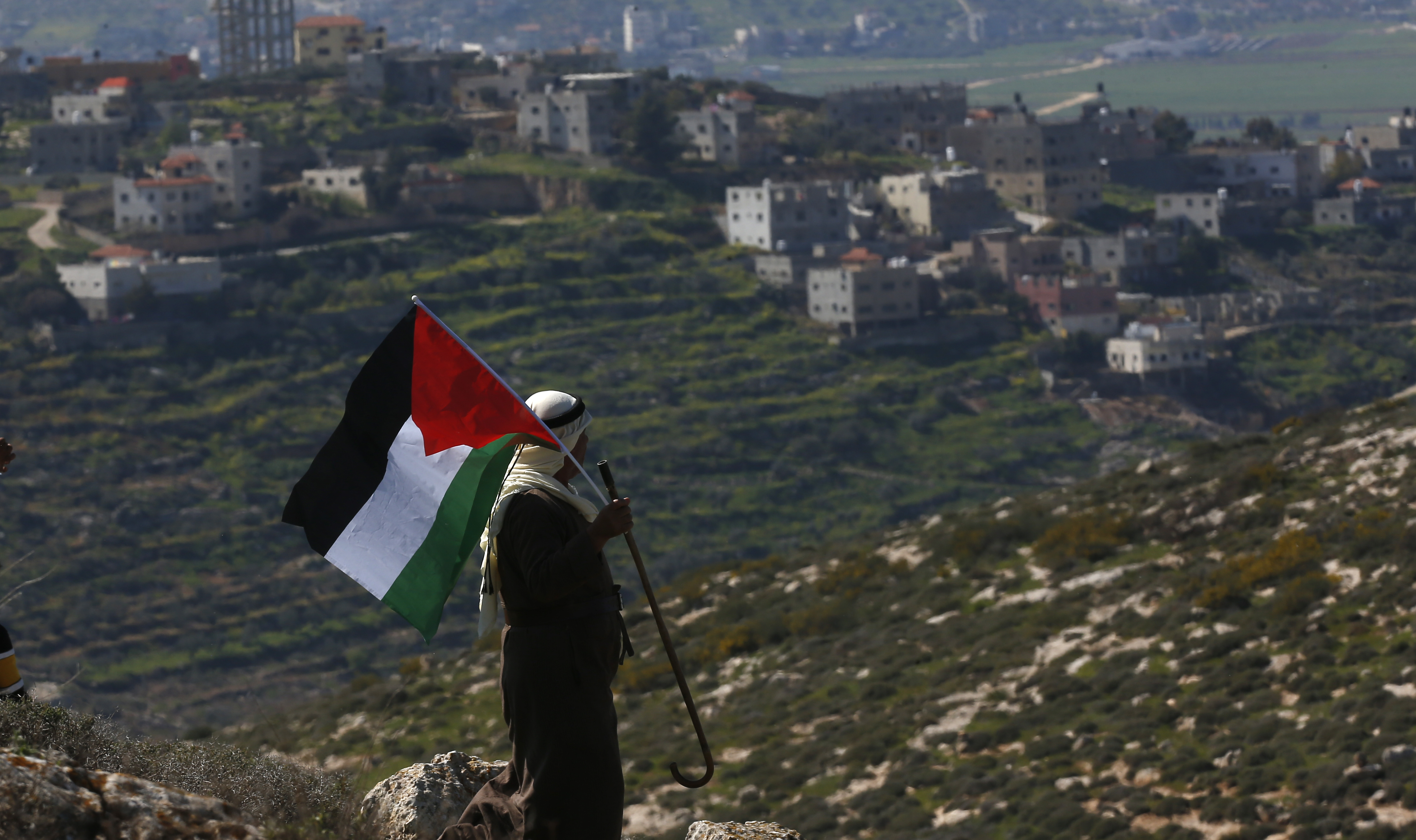epaselect epa09038334 A Palestinian man waves Palestine flag during a demonstration against Israel's settlements in the village of Bet Dajan near the northern West Bank city of Nablus, 26 February 2021.  EPA-EFE/ALAA BADARNEH