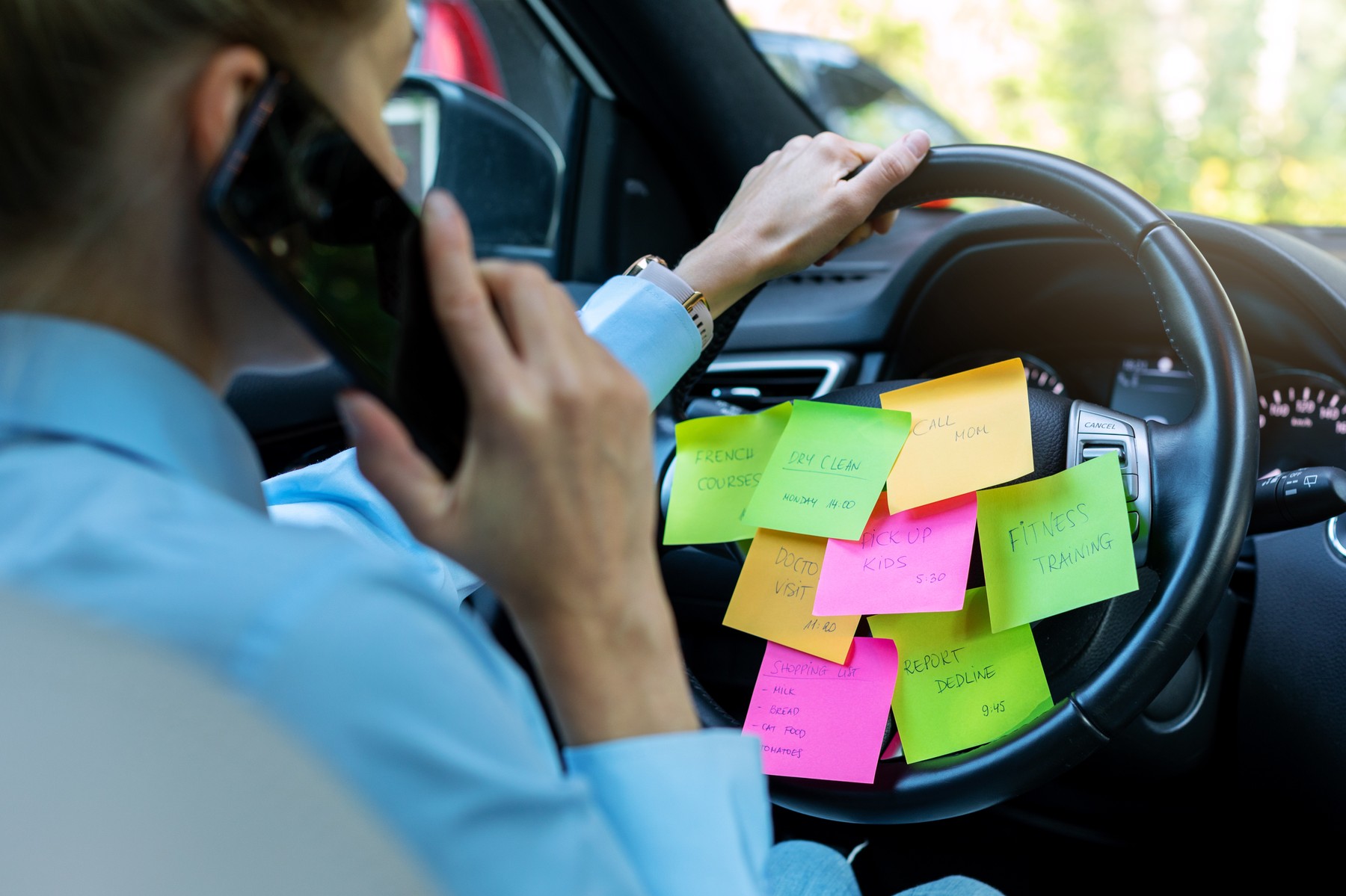 busy day schedule concept - woman driving car with to do list notes on the wheel and talking on the phone