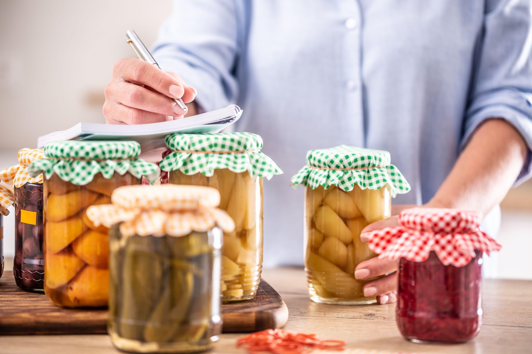Homemade preserved fruit and pickled vegetable with a woman writing down the recipe in the background.