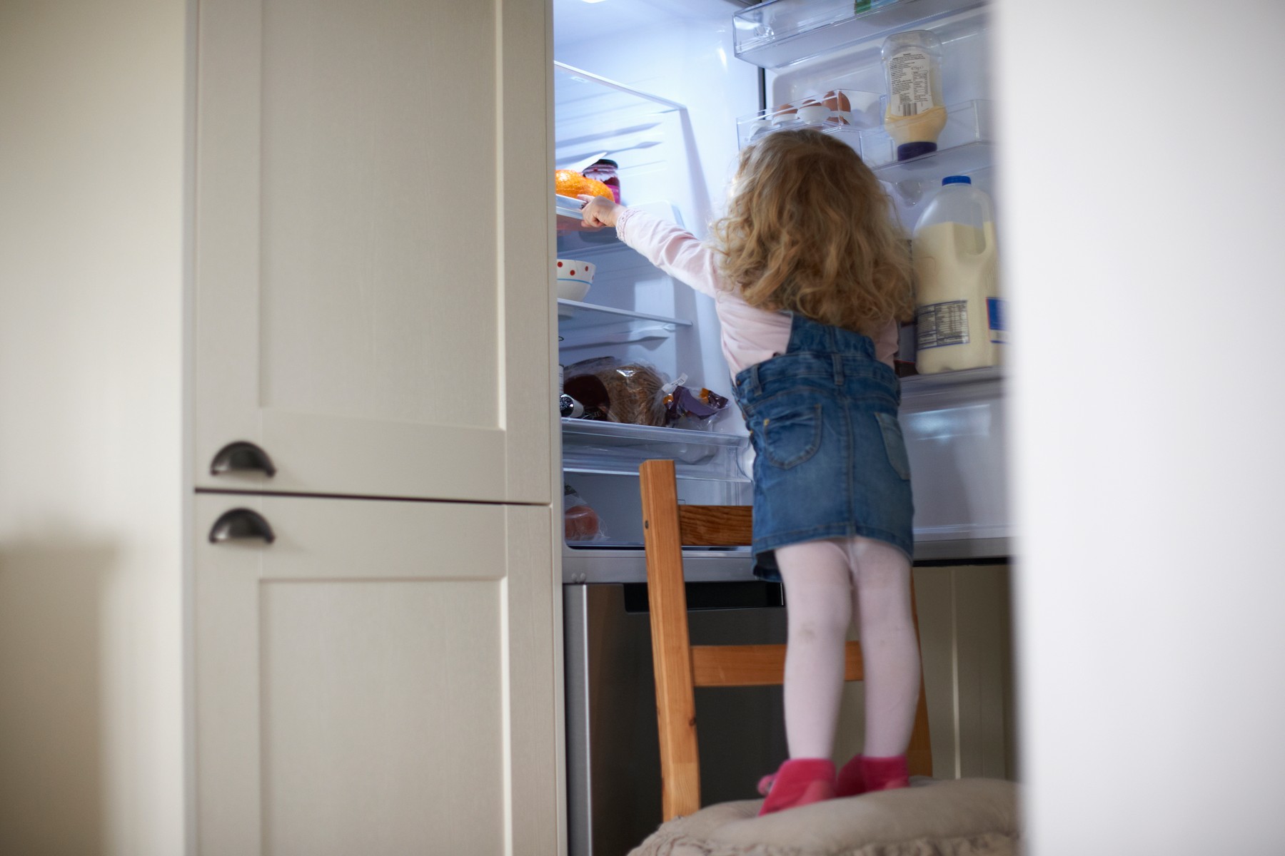 Young girl standing on chair, reaching into fridge, rear view