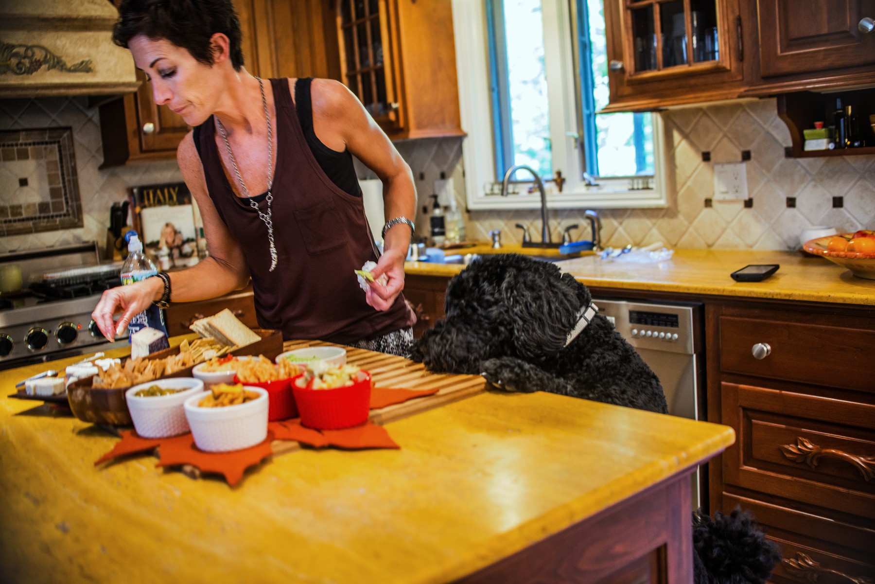 Woman preparing snacks at kitchen counter watched by pet dog
