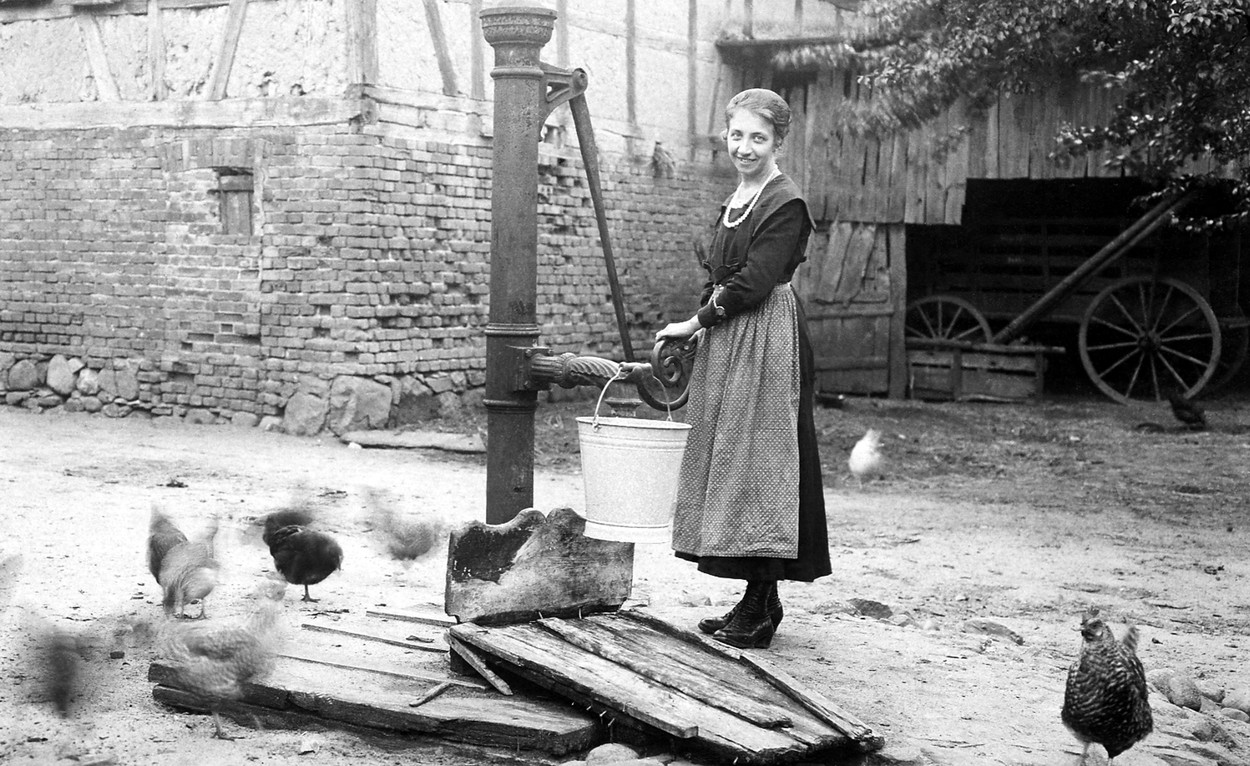Bäuerin holt Wasser von Wasserpumpe
