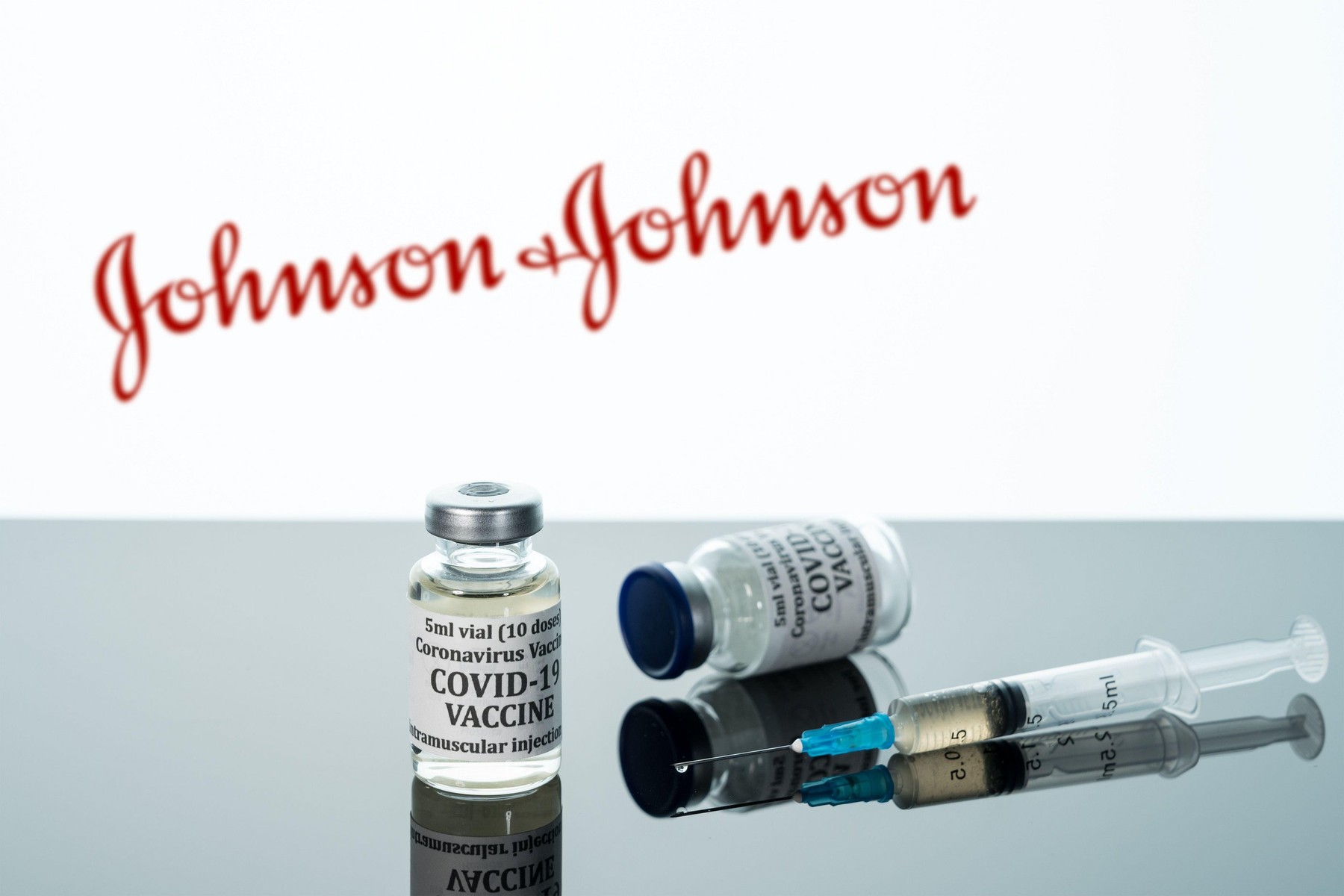 Morgantown, WV - 16 December 2020: Small bottle of coronavirus vaccine with syringe with background of Johnson and Johnson logo