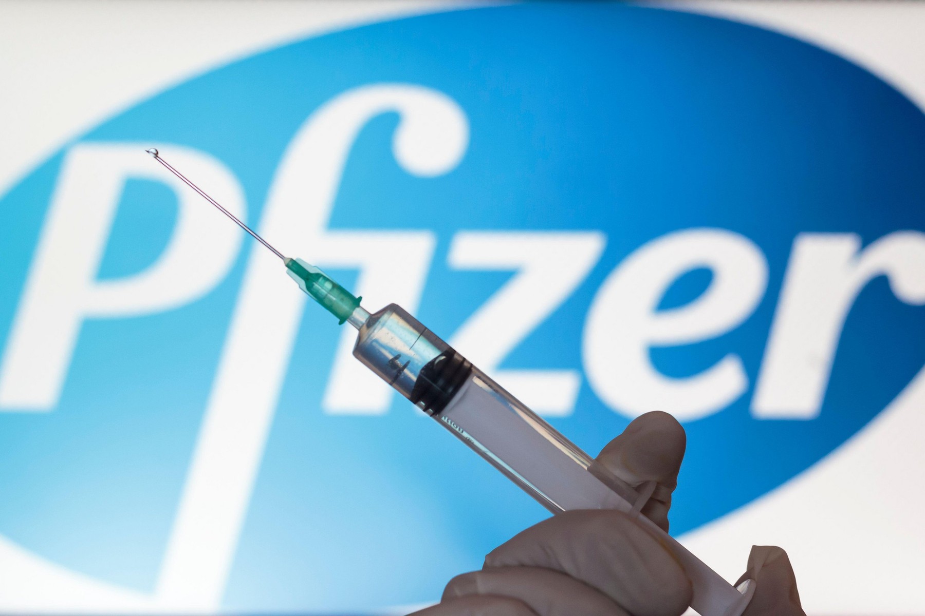 Lisbon, Portugal - November 22, 2020: Syringe and Pfizer logo on the background. Coronavirus, Covid-19 vaccine concept