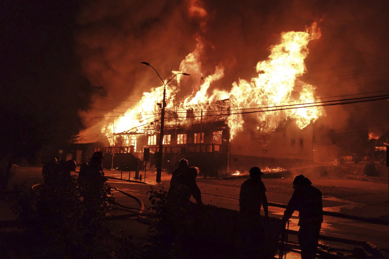 Firefighters work to fight a blaze at the mayor's office set on fire during a protest against the shooting of a street juggler killed by police during an identity check, in Panguipulli, Chile, Friday, Feb. 5, 2021. (Alicia Caceres/Aton Chile via AP)