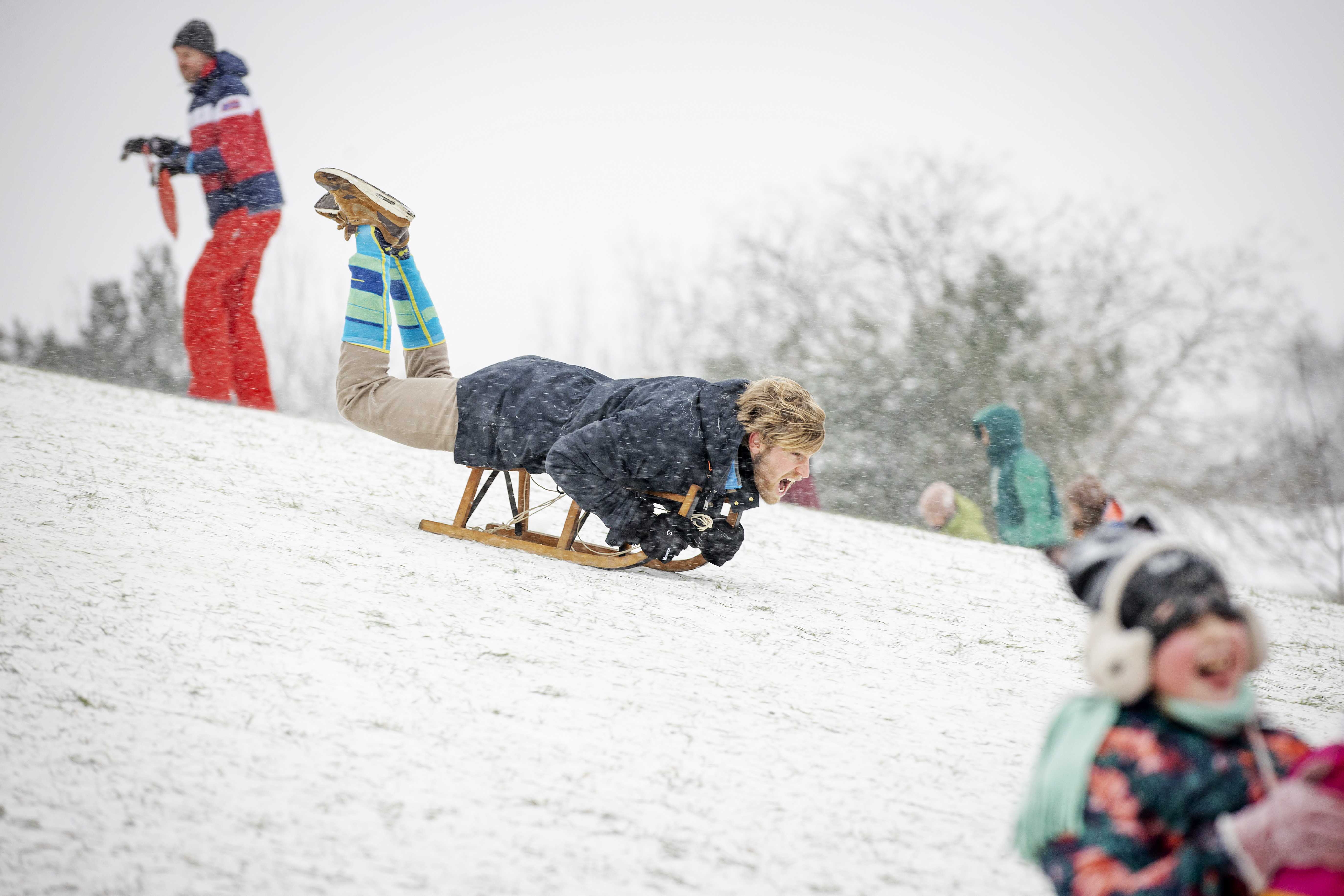 epa08993830 A man enjoys sledding in the snow in the Griftpark in Utrecht, The Netherlands, 07 February 2021. After ten years there is officially a snow storm in The Netherlands.  EPA-EFE/ROBIN VAN LONKHUIJSEN