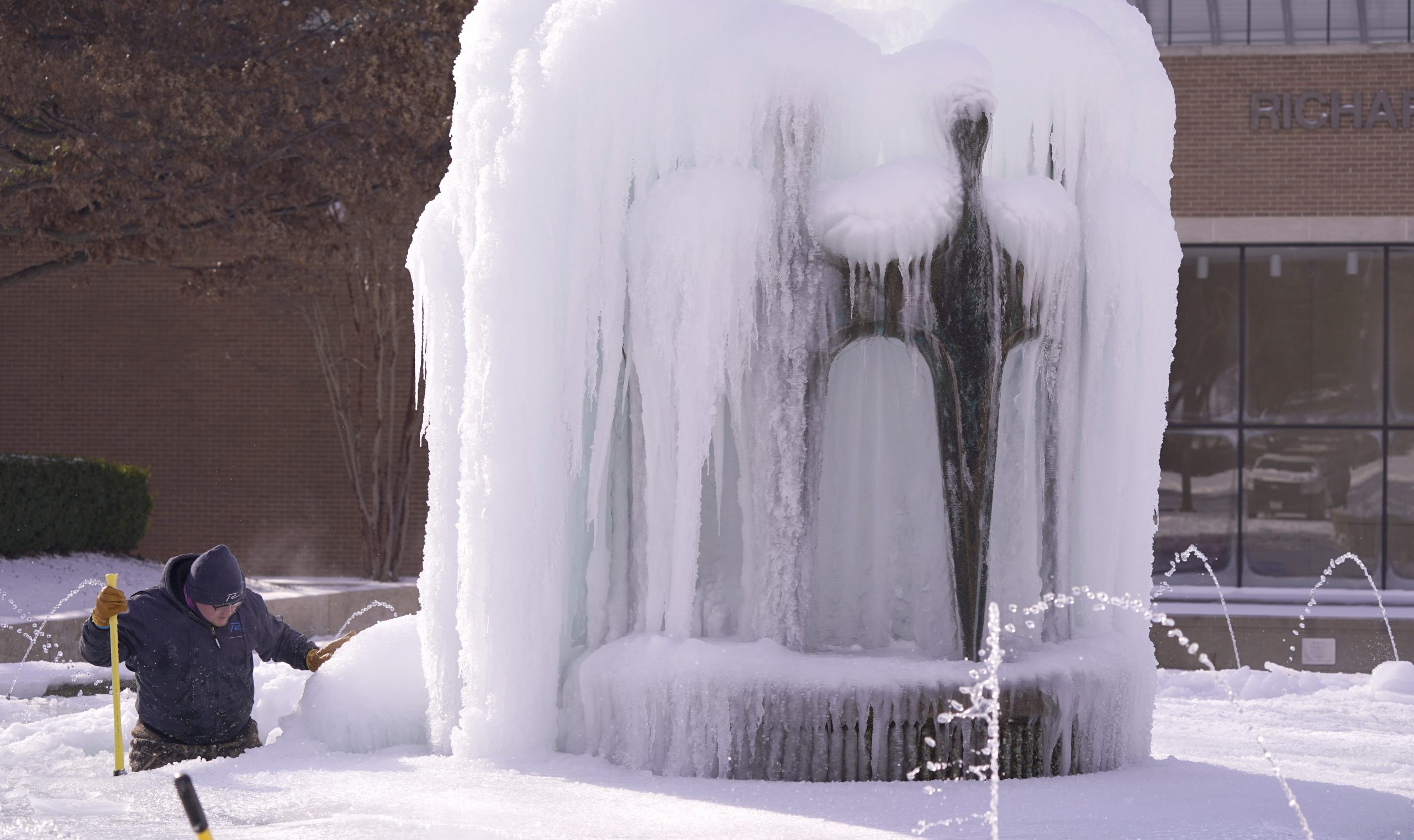 City of Richardson worker Kaleb Love works to clear ice from a water fountain Tuesday, Feb. 16, 2021, in Richardson, Texas.   Temperatures dropped into the single digits as snow shut down air travel and grocery stores. (AP Photo/LM Otero)