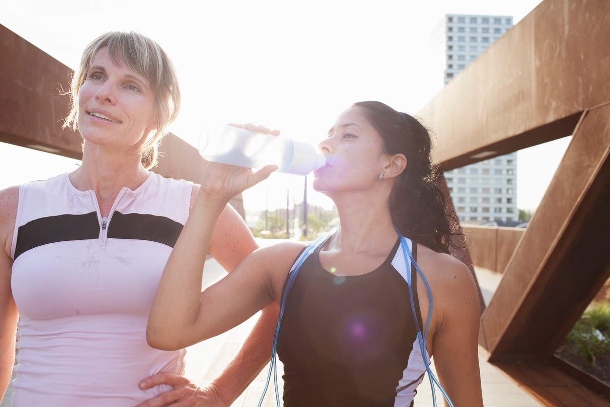 Two women taking a water break from training on urban footbridge