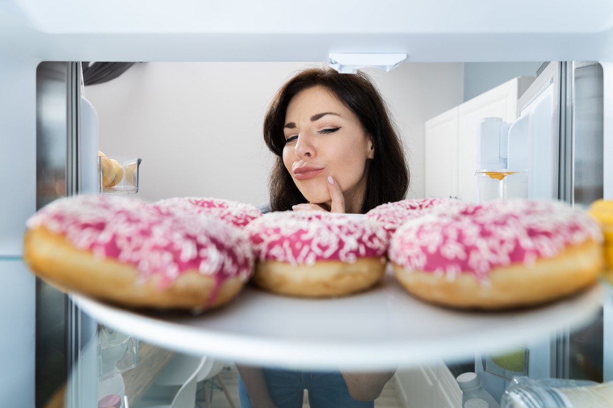 Confused Woman Thinking Looking At Sweets In Fridge