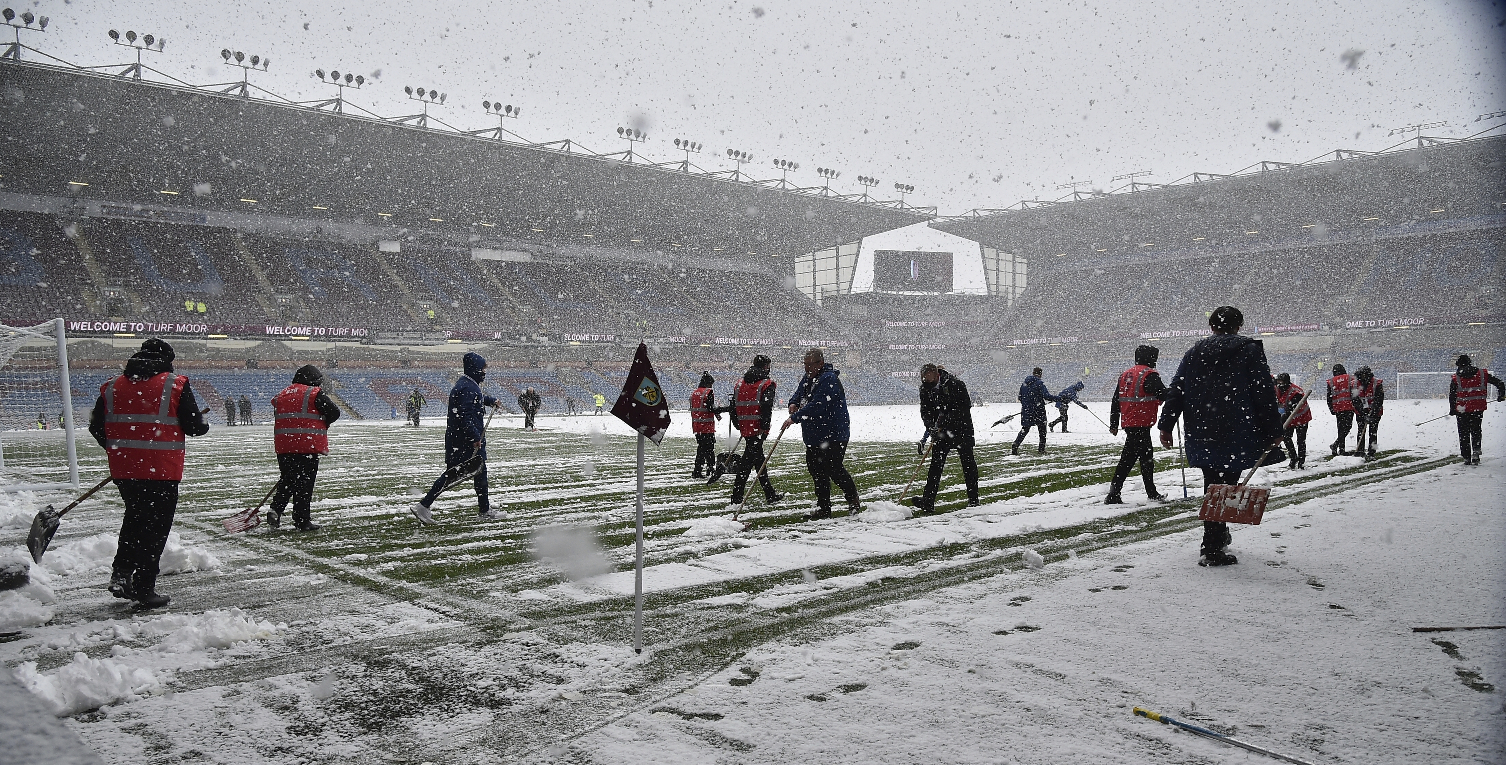 Staff workers clean snow from the pitch before the Premier League soccer match between Burnley and Tottenham Hotspur at Turf Moor, in Burnley, England, Sunday, Nov. 28, 2021. (AP Photo/Rui Vieira)