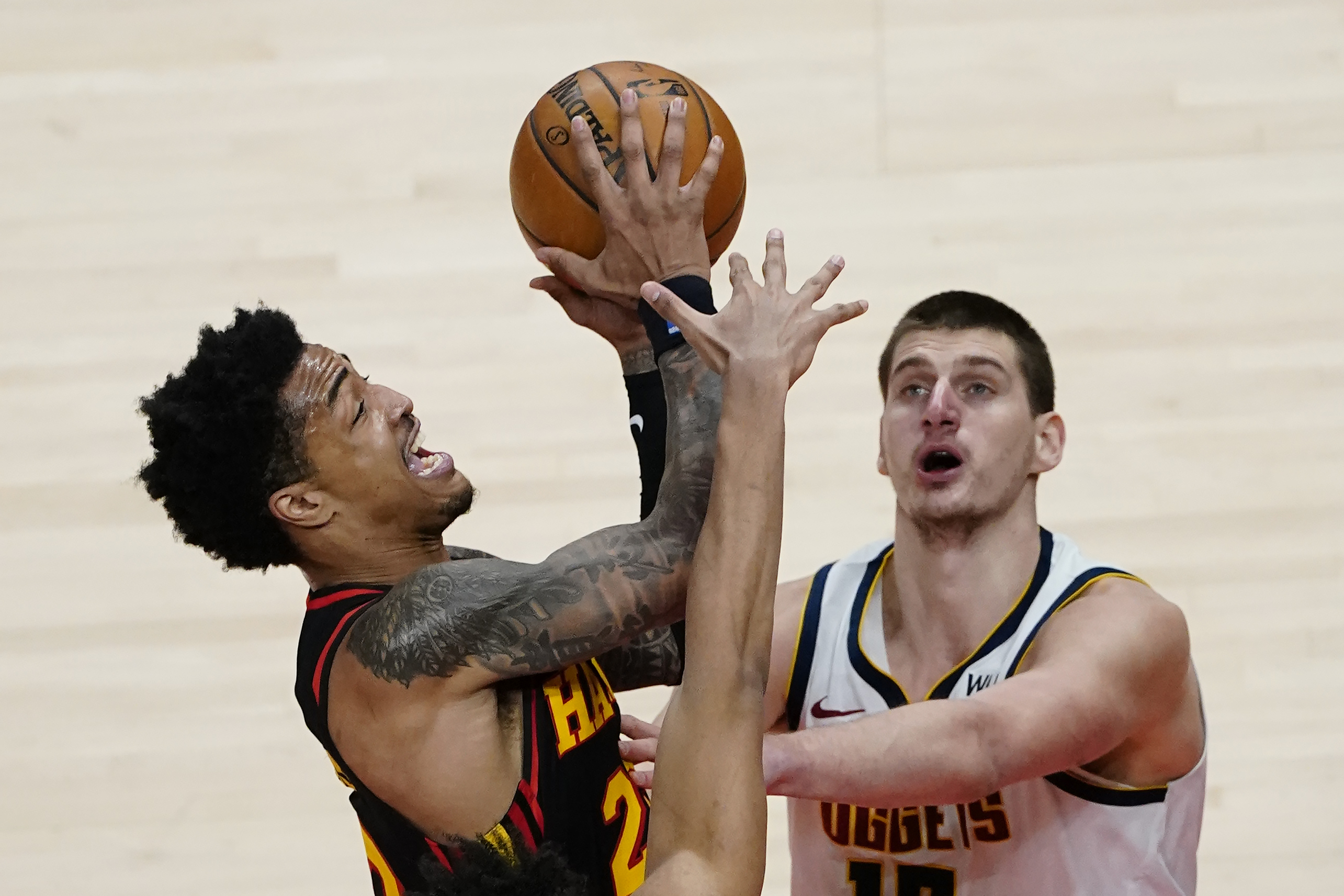 Atlanta Hawks forward John Collins, left,  goes in for a basket as Denver Nuggets center Nikola Jokic, right,  defends during the second half of an NBA basketball game Sunday, Feb. 21, 2021, in Atlanta. (AP Photo/John Bazemore)