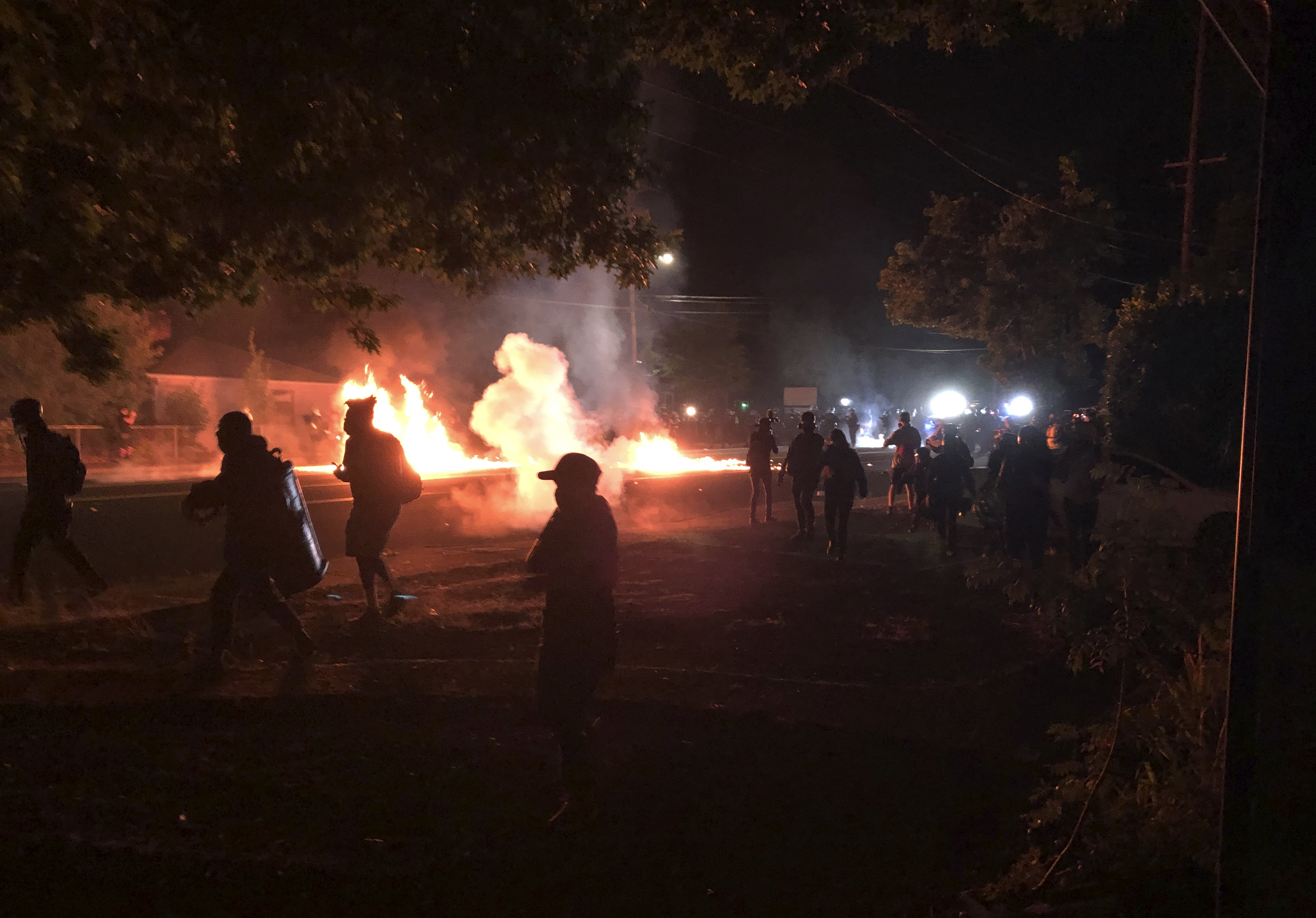 Flames rise from a street after a liquid had been spread and lit, Saturday, Sept. 5, 2020, during protests in Portland, Ore. Some protesters, at, left, move back as police, at background right, advance. (AP Photo/Andrew Selsky)