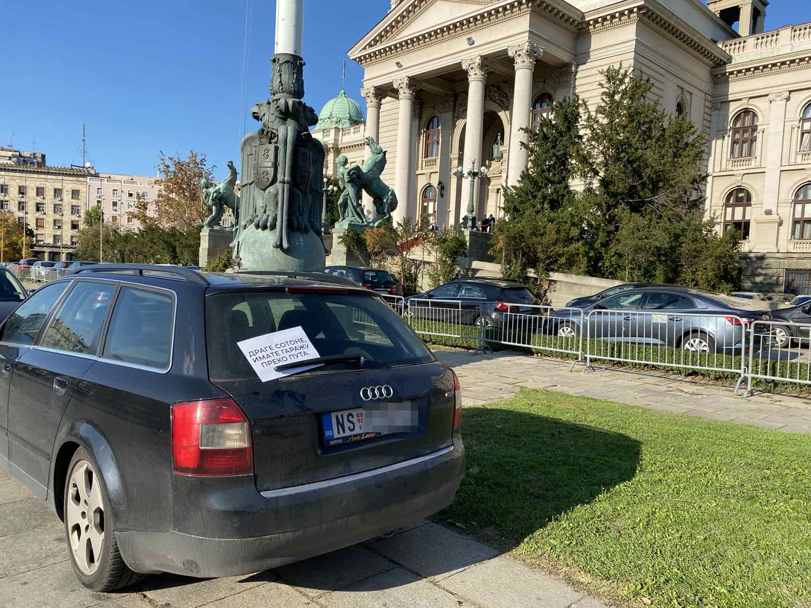 Bahato parkirani automobili ispred skupstine Srbije, na njih je neko nakacio papir sa natpisom " Drage sotone imate garazu preko puta "