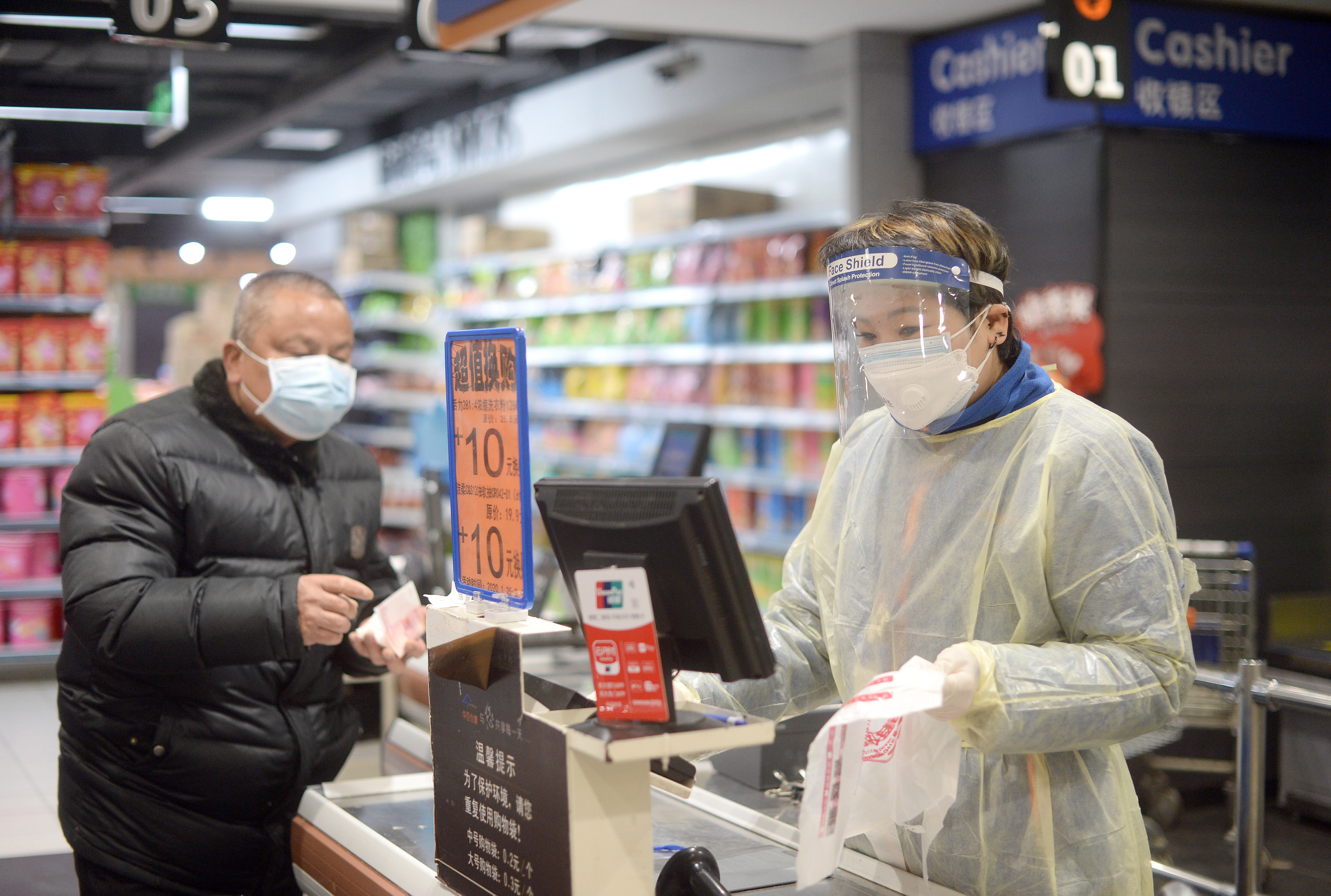 epa08208914 A cashier in a plastic gown works at the checkout of a supermarket in Wuhan, the epicenter of the novel coronavirus outbreak, in central China's Hubei province, 10 February 2020.