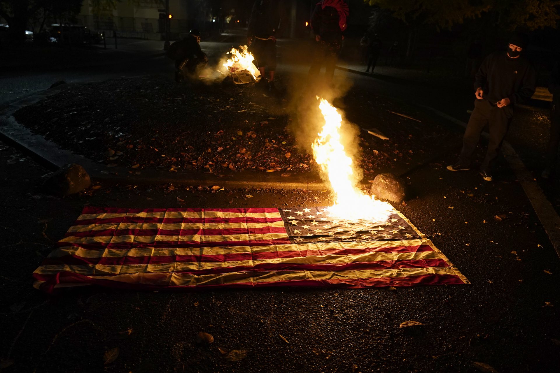 People watch as a flag burns outside of the Mark O. Hatfield United States Courthouse after a march on the night of the election, Tuesday, Nov. 3, 2020, in Portland, Ore. (AP Photo/Marcio Jose Sanchez)