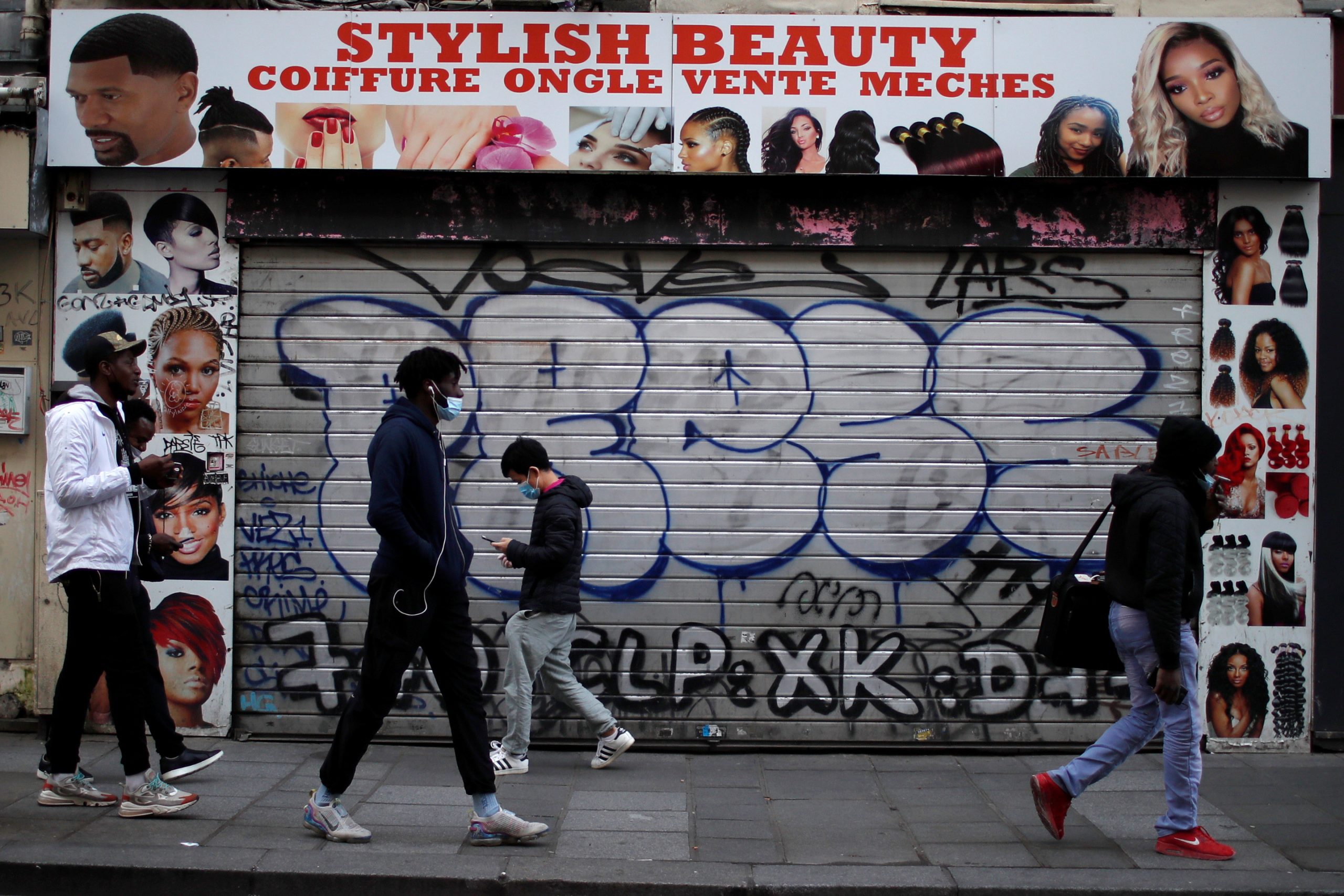 People, wearing protective face masks, walk past a closed beauty shop in a street in Paris during the second national lockdown as the coronavirus disease (COVID-19) outbreak continues in France, November 19, 2020. REUTERS/Gonzalo Fuentes