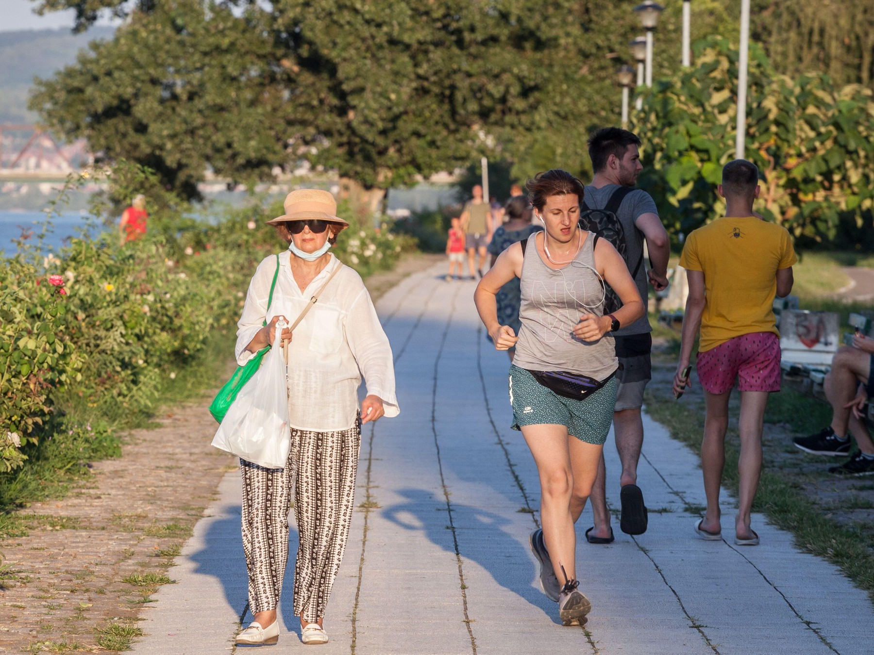 BELGRADE, SERBIA - AUGUST 29 2020: Old woman wwalking with a facemask while a younger girl works out runs next to her without face mask protective equ