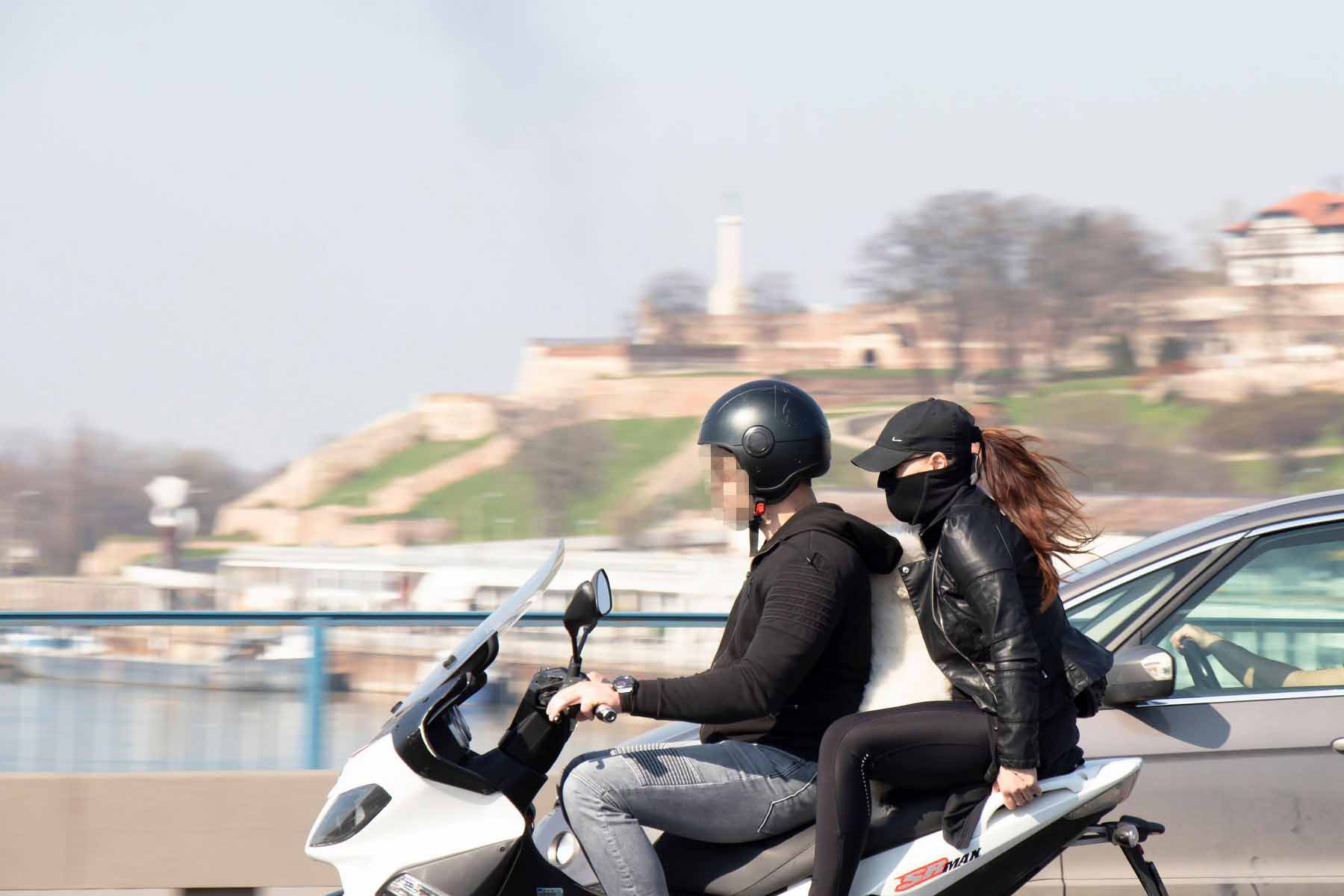 Belgrade, Serbia - March 19, 2020 : A couple riding on a scooter with a dog in the middle on the highway bridge, with Kalemegdan fortress behind them
