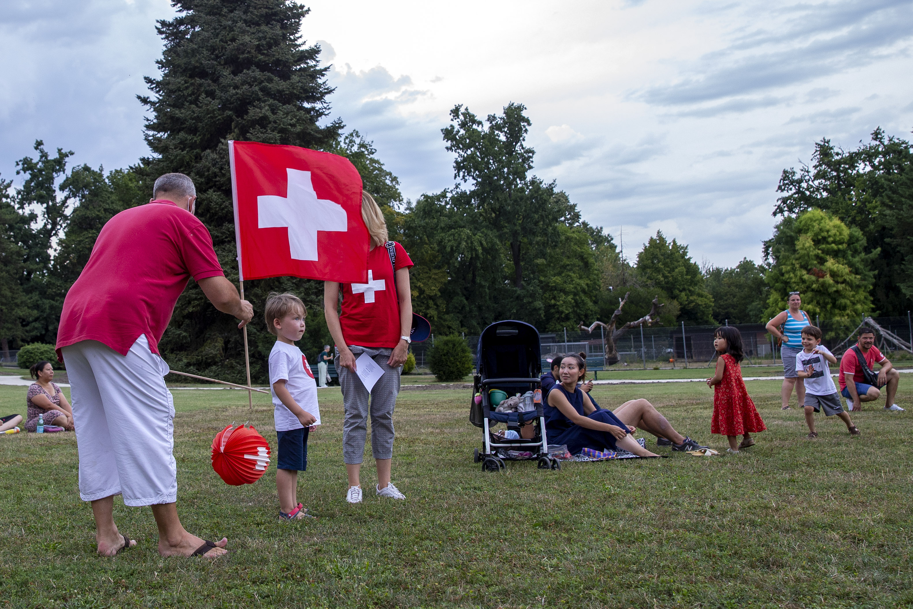 epa08579710 A men fixes up a lantern with the Swiss colors and a Swiss flag next to his family during the Geneva's official ceremony of the Swiss National Day, in Geneva, Switzerland, 01 August 2020.  EPA-EFE/SALVATORE DI NOLFI